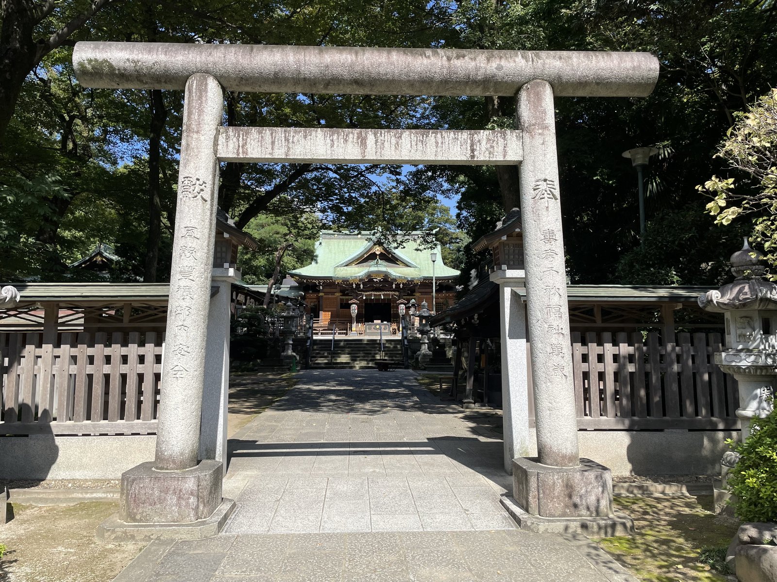 石の鳥居の向こうに、緑の屋根の拝殿が木立に囲まれて見える大鷲神社の境内