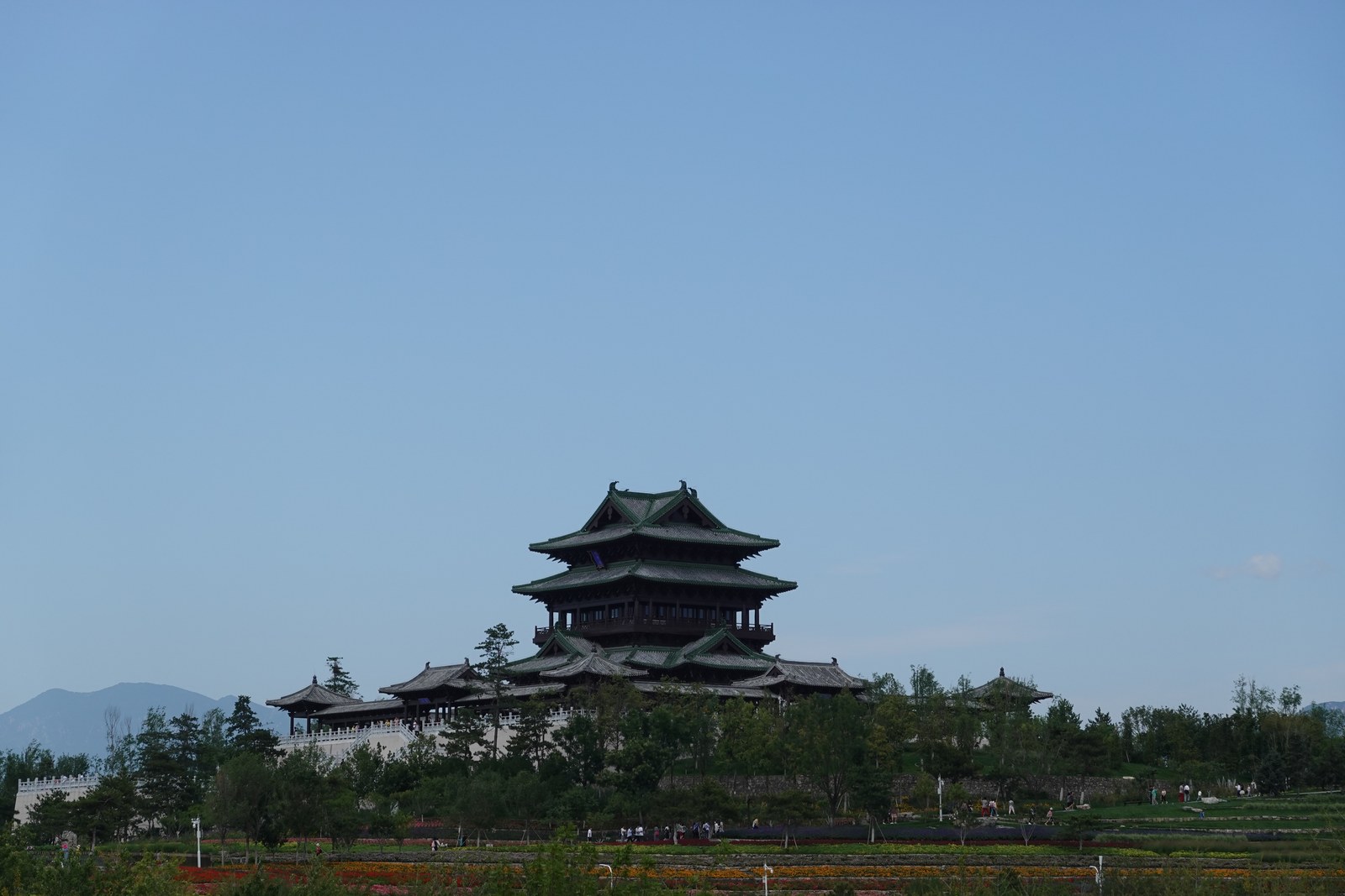 北京世界園芸博覧会の会場に立つ永寧閣。丘の上の木造の楼閣が青空にそびえ、手前に花畑が広がる