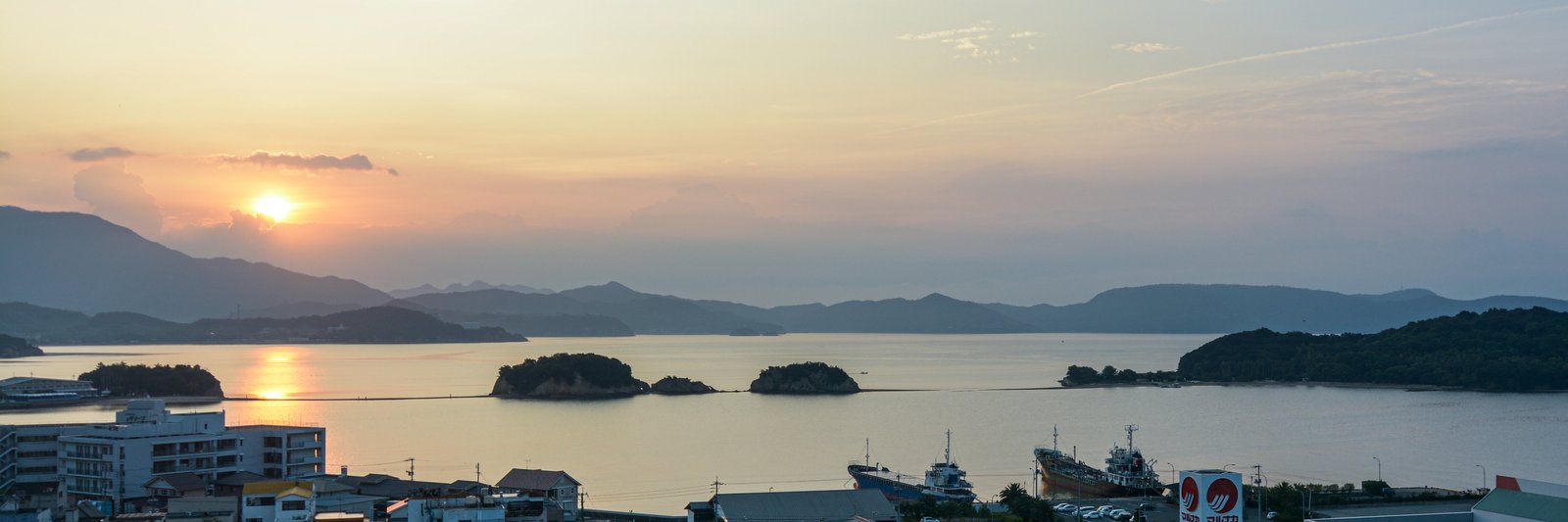 夕方の土庄の海。手前に町並みと港に泊まる船、沖に小さな島が並び、島と島の間に細い砂州が見える