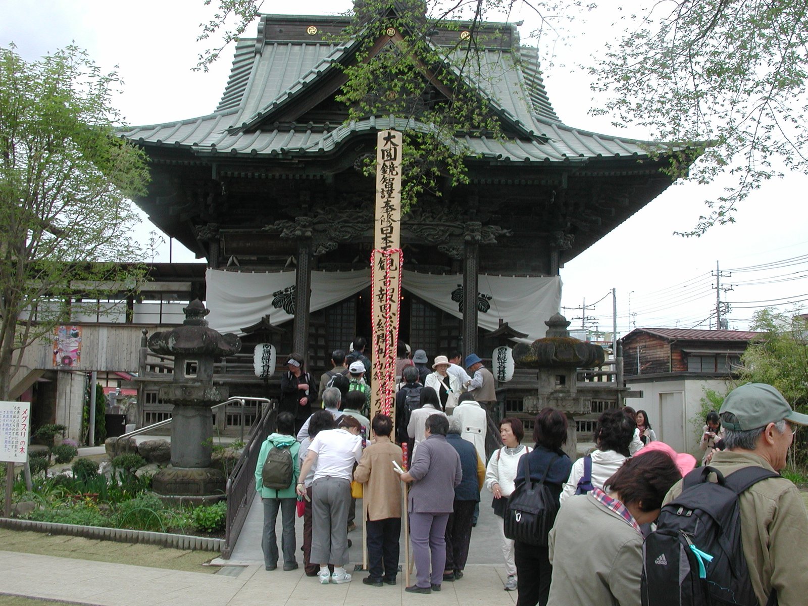 秩父札所13番 慈眼寺の観音堂。銅板葺きの屋根の堂の前に「日本百観音報恩総開帳」と書かれた木の柱が立ち、参拝者が並んでいる