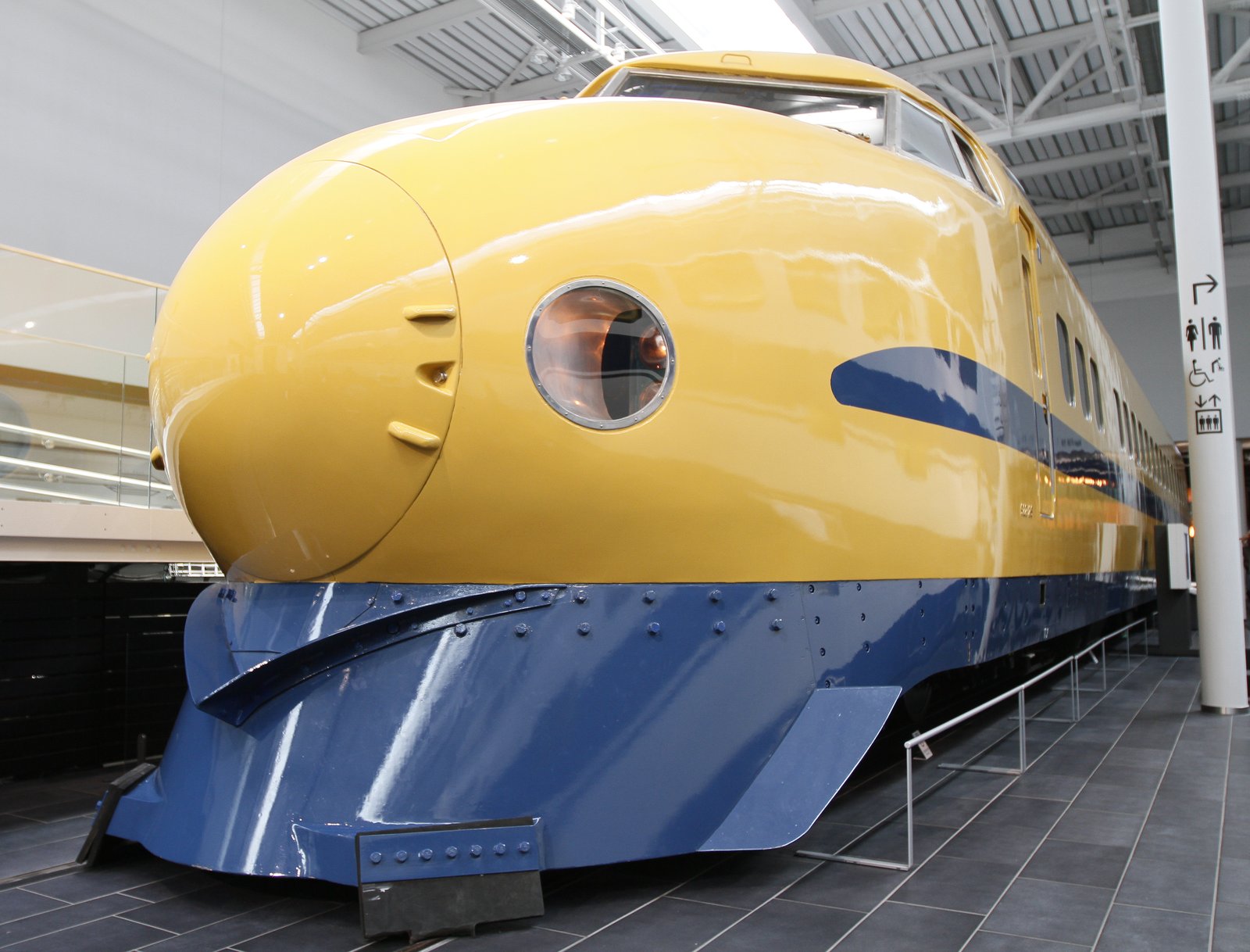 博物館の館内に置かれた黄色い車体に青い帯の922形の先頭車。丸い鼻先に丸窓のライトがあり、車体の下半分が濃い青