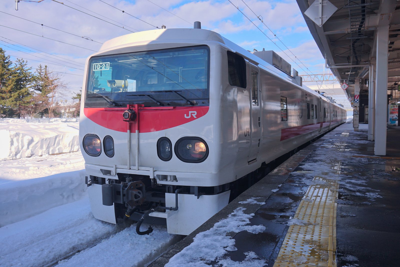 雪の残る駅のホームに停車する白い車体に赤い帯の気動車。先頭の窓に「ID-21」の表示、前面に測定用のカメラ
