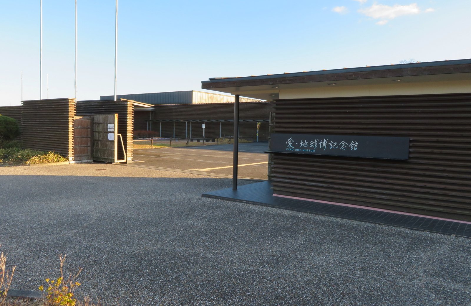愛・地球博記念館の入口。横板張りの焦げ茶の壁に「愛・地球博記念館 EXPO 2005 MUSEUM」の黒い看板が掛かり、奥に木の門と平屋の建物が見える