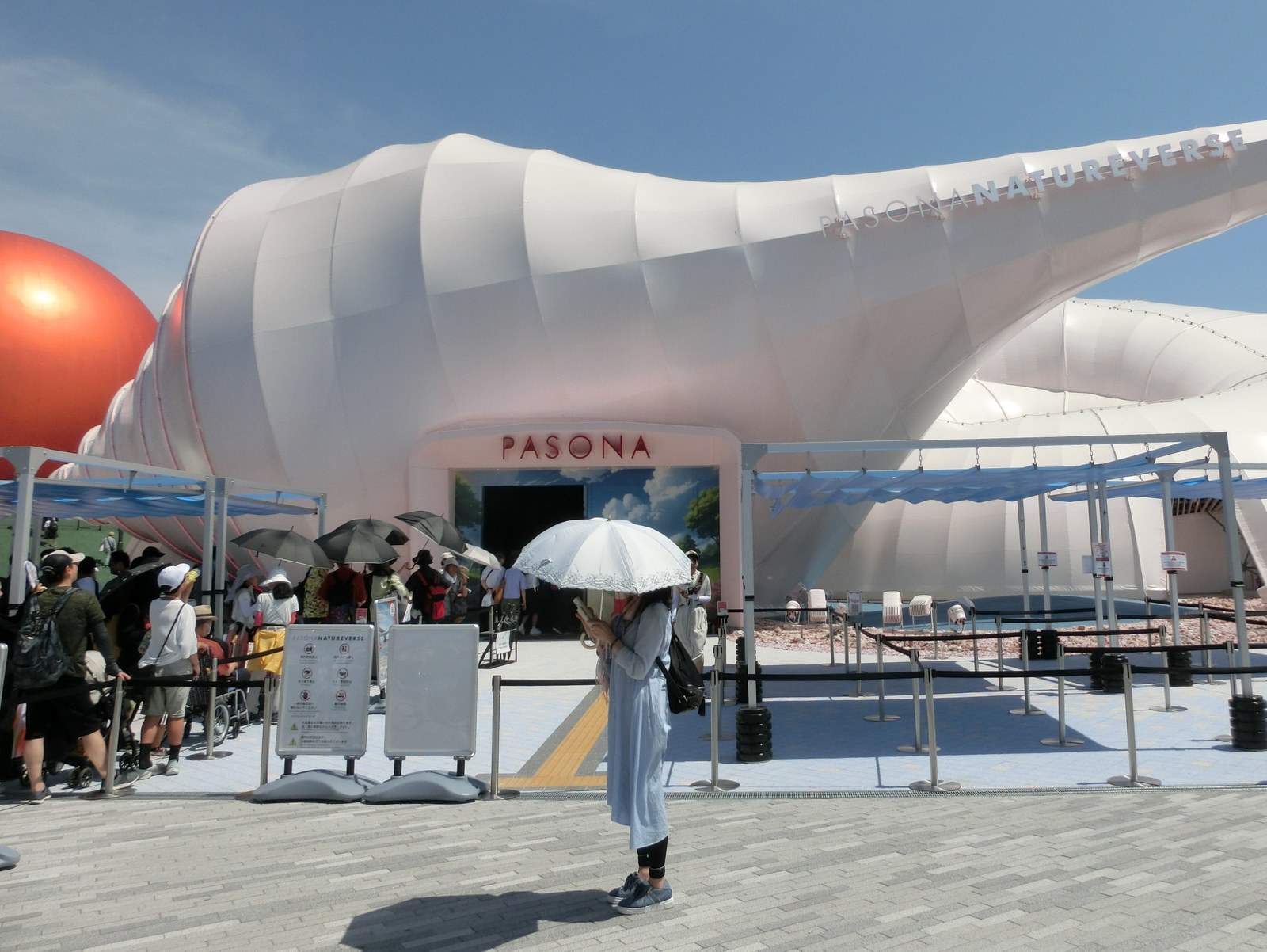 大阪・関西万博のパソナ館「PASONA NATUREVERSE」。白い貝殻のような膜の建物の入口に来場者の列ができ、左奥に赤い球体が見える