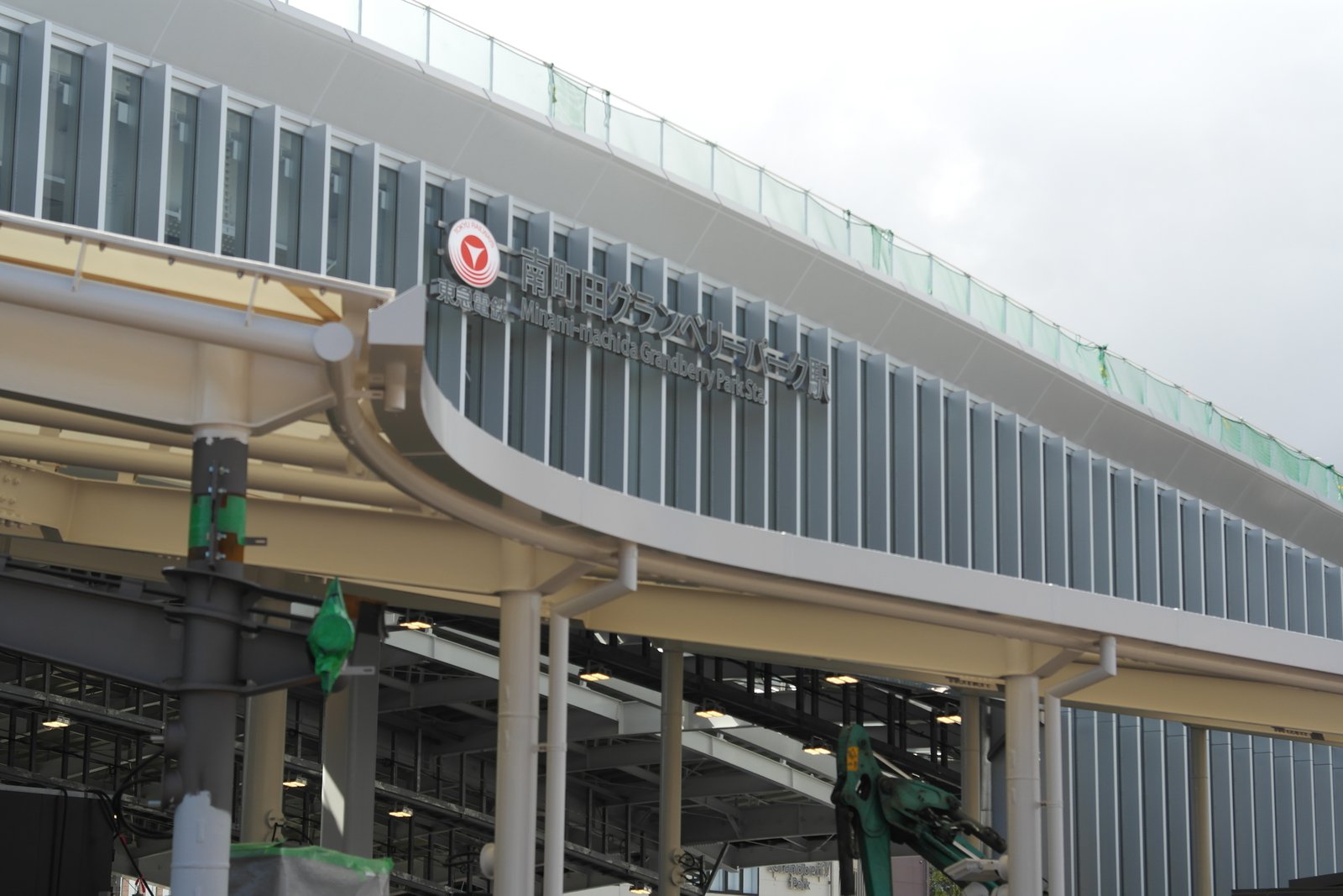 南町田グランベリーパーク駅の北口。白い曲線の屋根の上の壁に東急電鉄のマークと駅名の文字があり、手前に工事の重機が見える