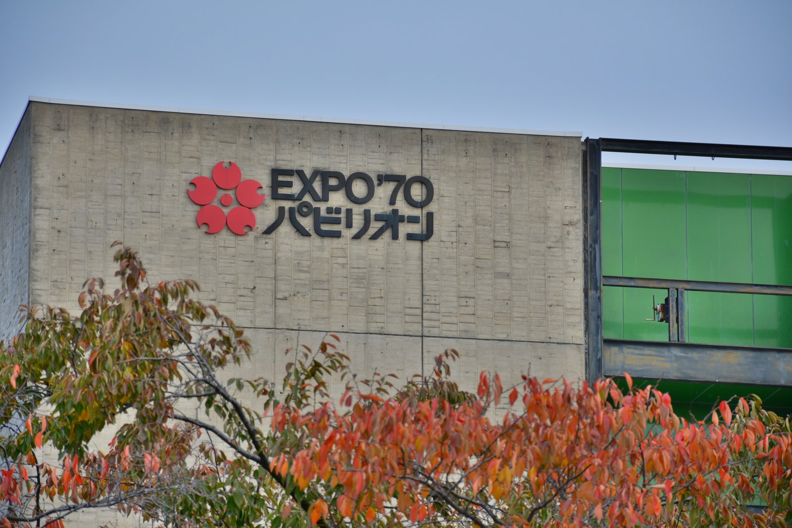 EXPO'70パビリオンのコンクリートの壁の上部。桜の花の形のシンボルマークと「EXPO'70パビリオン」の文字、手前に色づいた木の葉