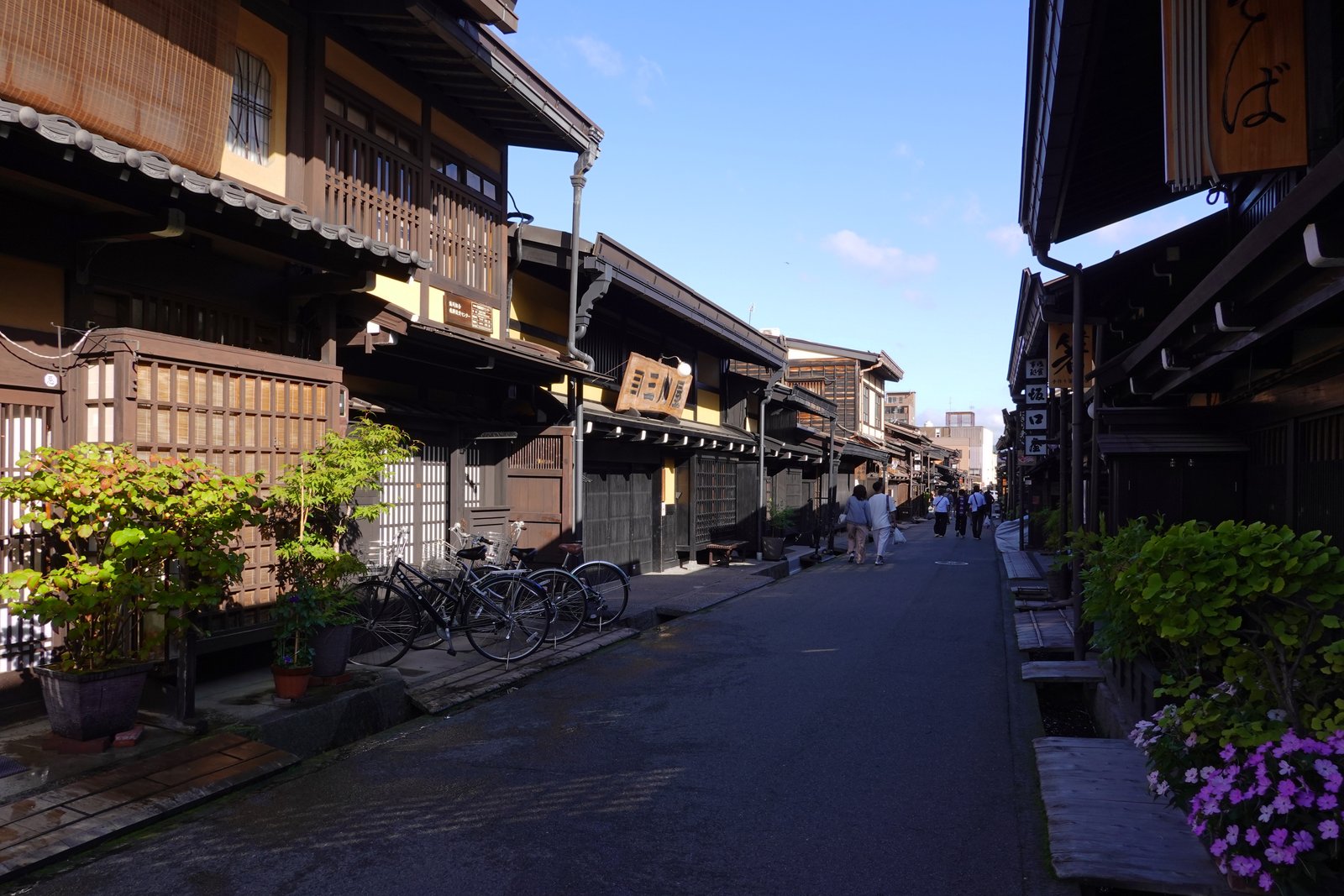 高山の三町の通り。黒っぽい木の格子と深い軒の町家が両側に並び、店の看板と自転車が軒先にある