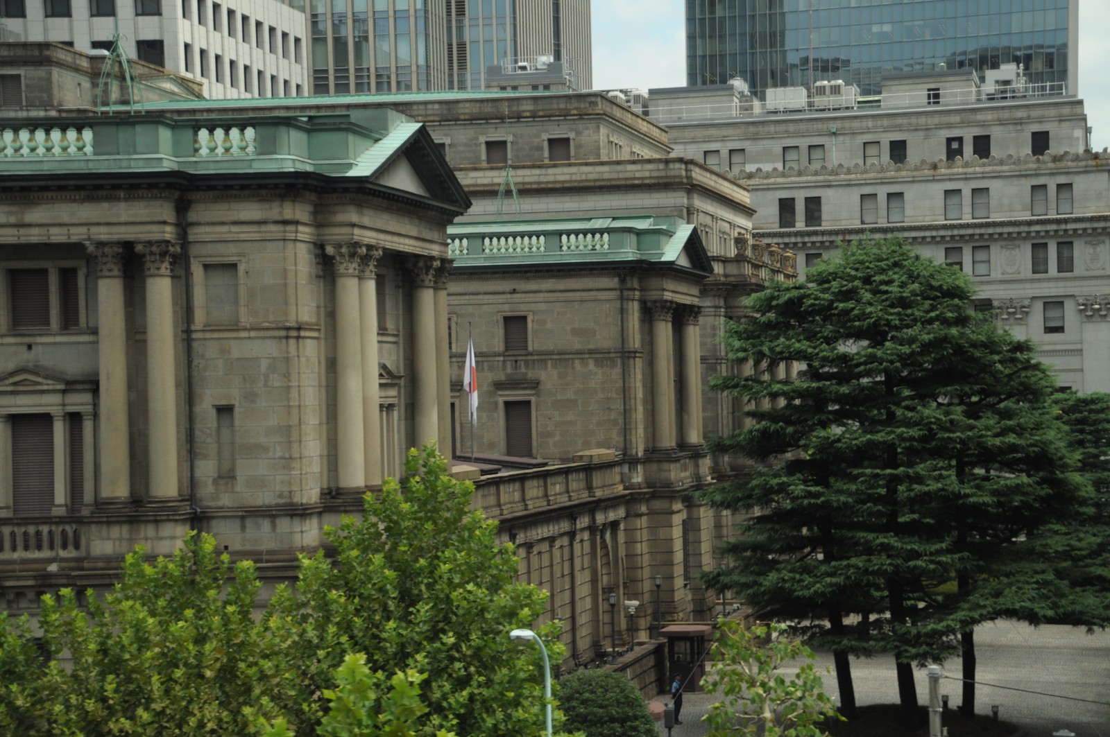 日本橋にある日本銀行本店旧館の外観。銅板葺きの丸屋根とコリント式の石柱が並ぶ石積みレンガ造りの建物で、手前に街路樹が茂る。