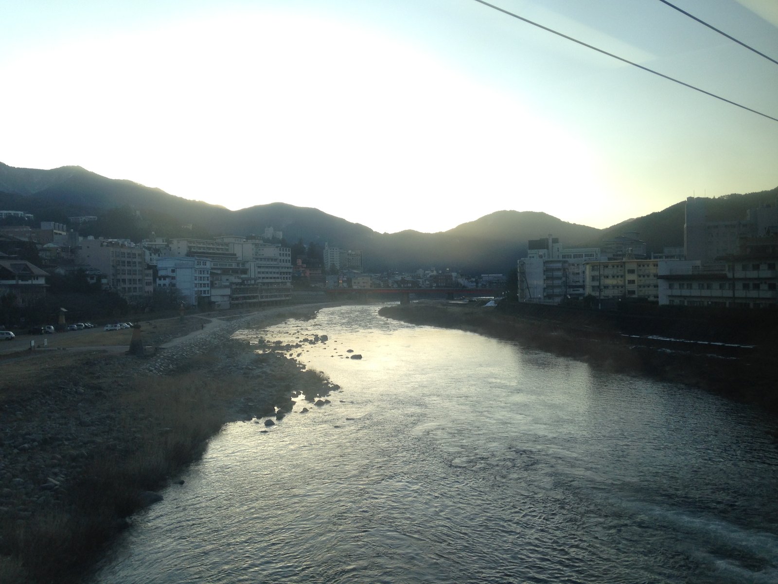 特急ひだの車窓から見た、飛騨川の川面と両岸に旅館が並ぶ下呂温泉街。奥に山並みと赤い橋が見える