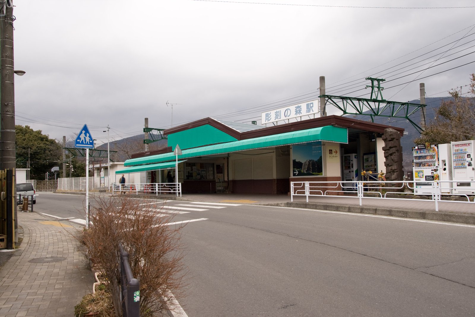 箱根登山鉄道の彫刻の森駅の駅舎。緑色の庇の付いた平屋の建物で、屋根の上に「彫刻の森駅」の看板が立ち、前を道路が通っている
