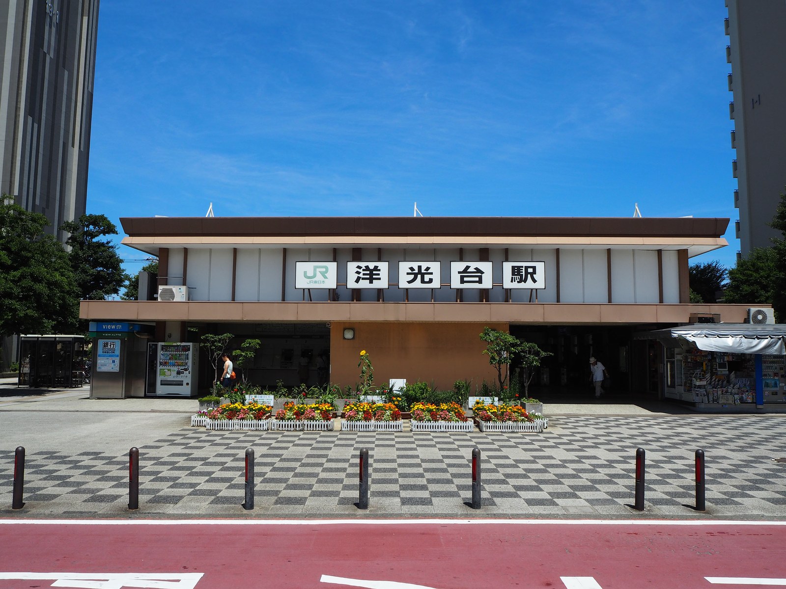 洋光台駅の駅舎正面。白い壁に「洋光台駅」の看板を掲げ、手前に花壇とチェック柄の広場がある