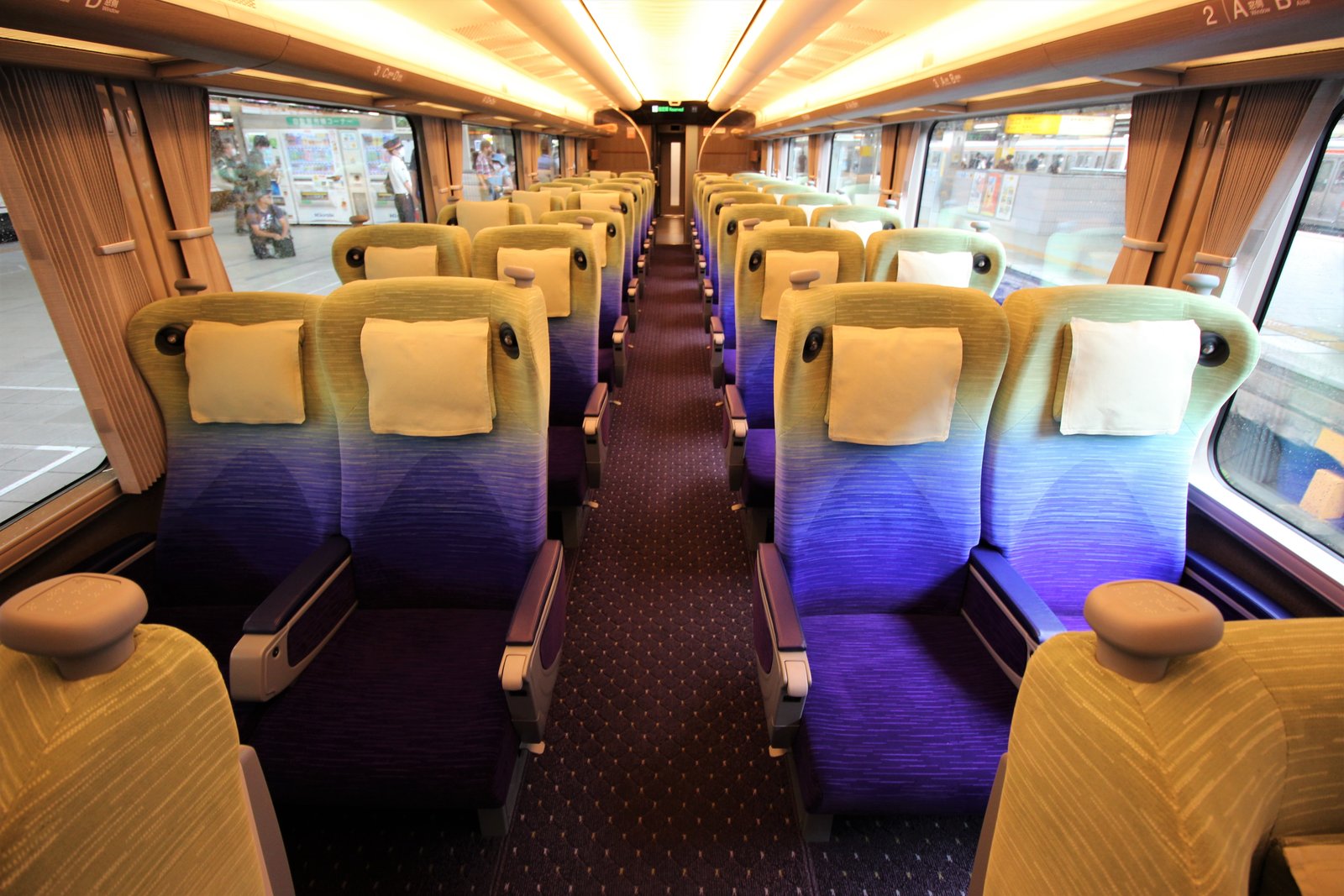 HC85系のグリーン車の車内。背もたれの上が黄緑、下が紫の座席が通路をはさんで2列ずつ並び、各席に白い枕カバーが掛かる