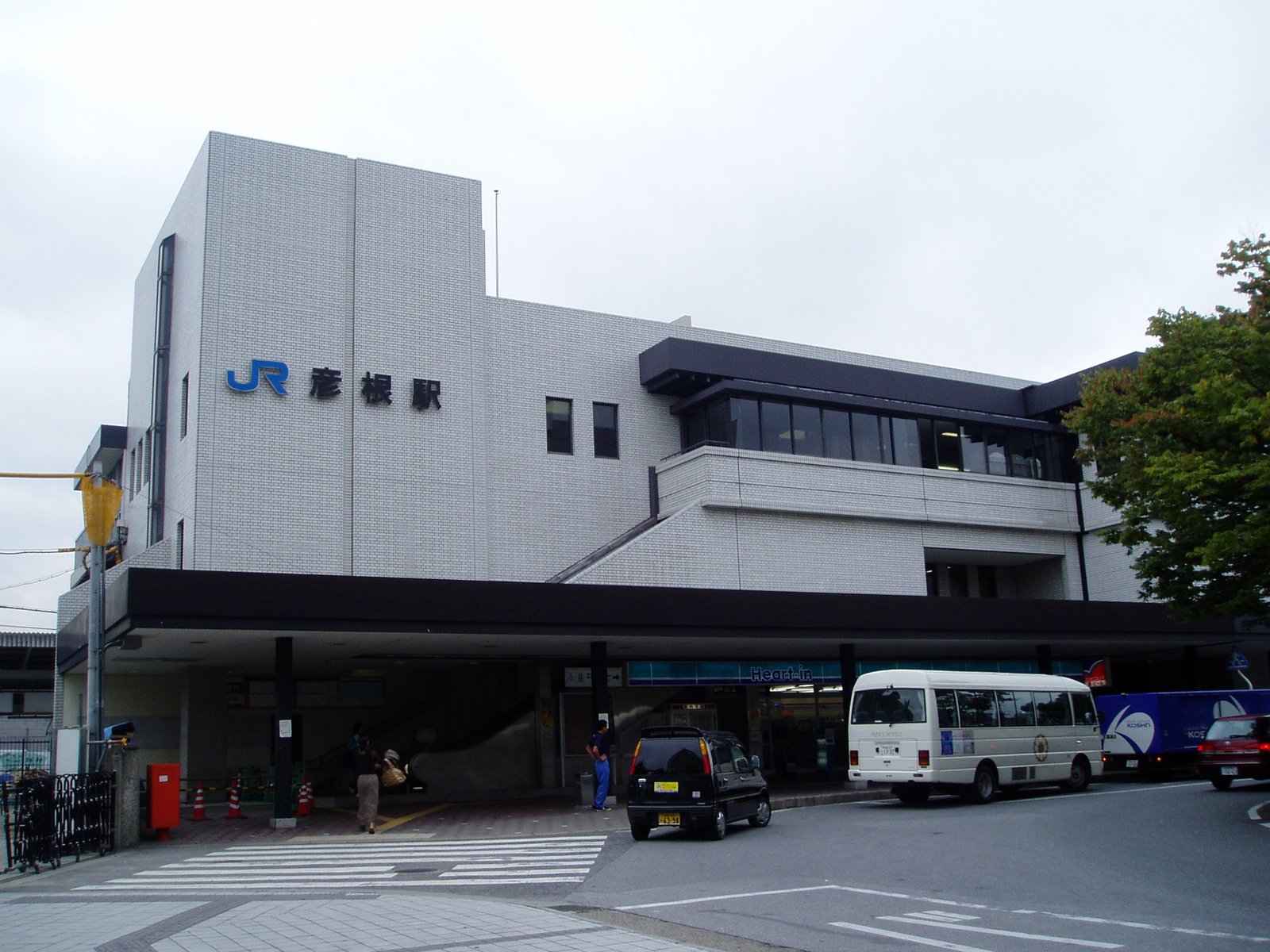 JR彦根駅の西口。白いタイル張りの駅舎に「JR 彦根駅」の文字が付き、1階の庇の下に改札へ上がる階段と店がある