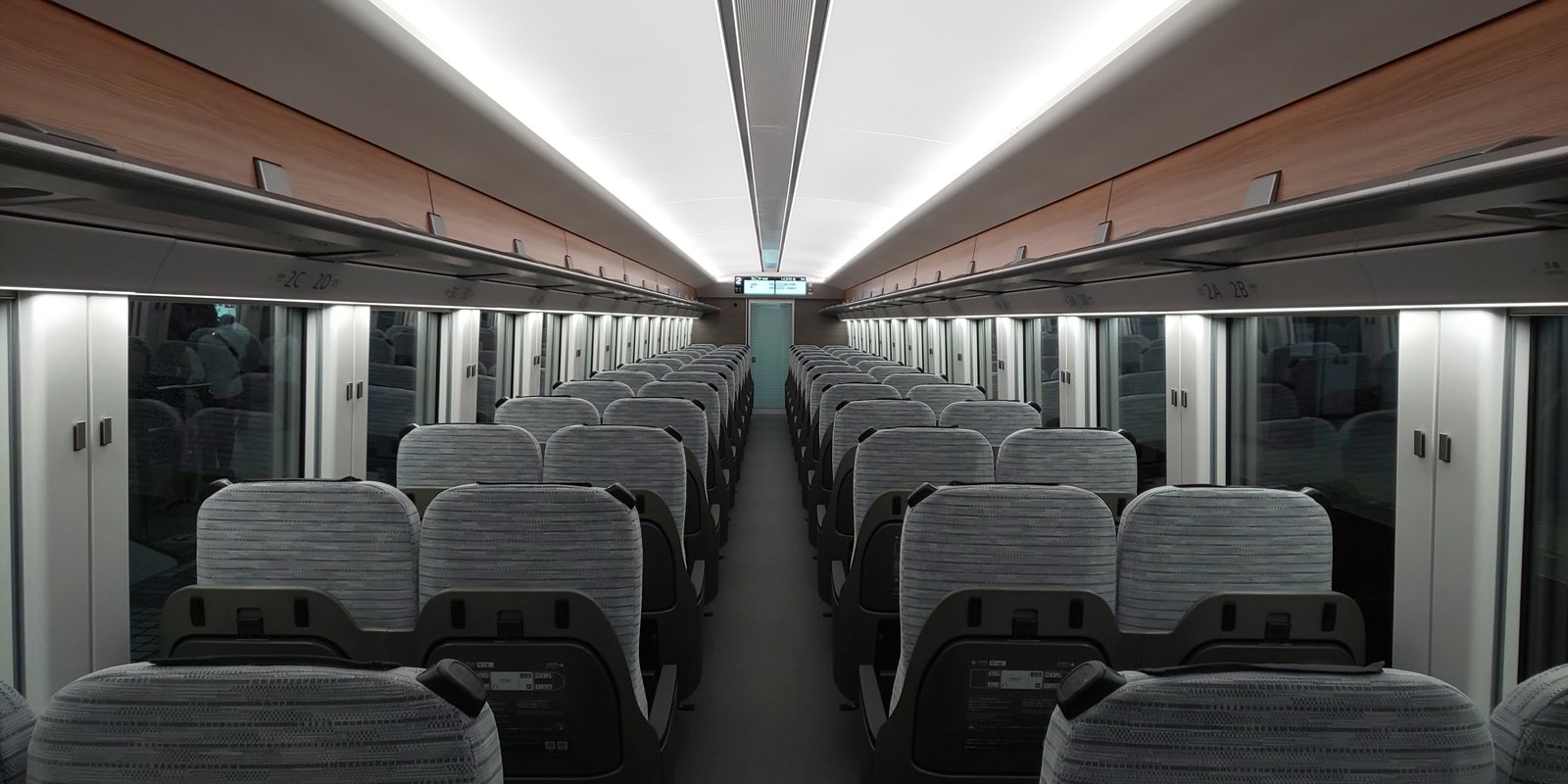 ひのとりのレギュラー車両の車内。グレーの布張りの座席が通路をはさんで2列ずつ並び、各席の背面にバックシェルが付く
