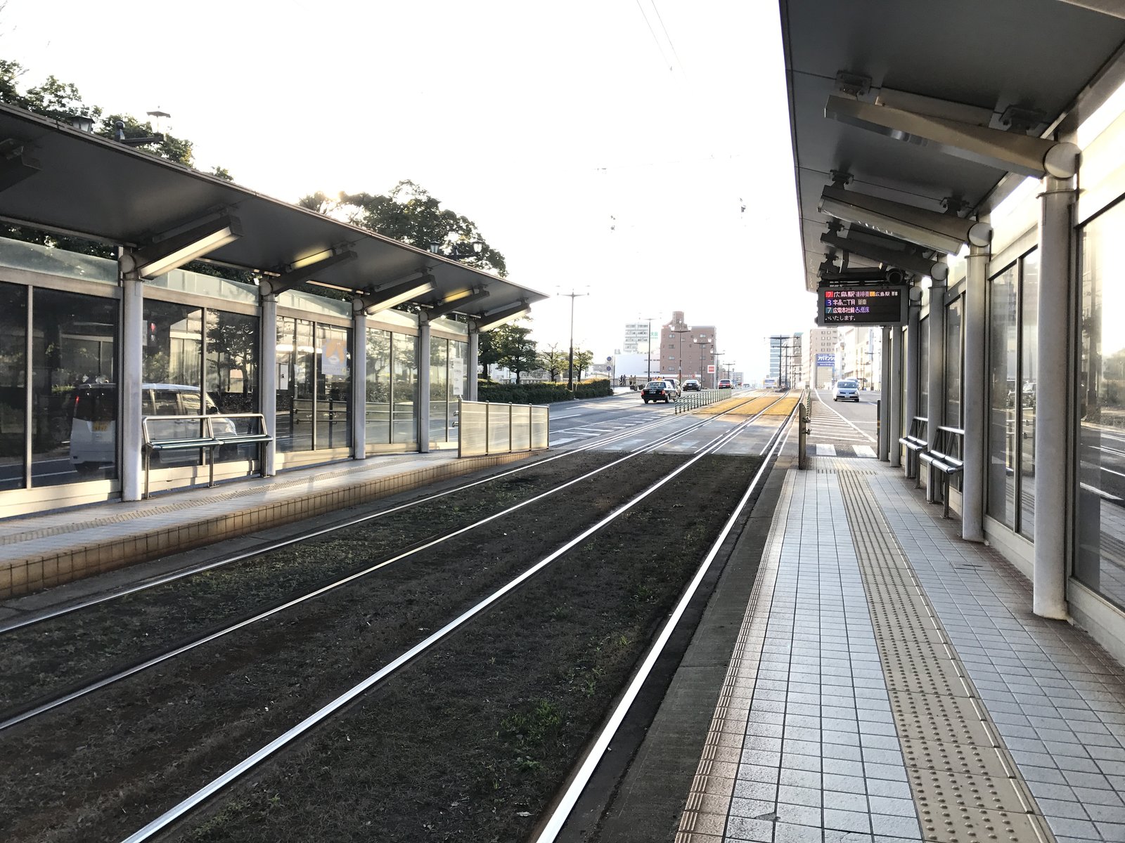 広島電鉄の原爆ドーム前停留場。線路をはさんで屋根付きのホームが左右に向かい合い、右のホームには電光表示の行先案内がある