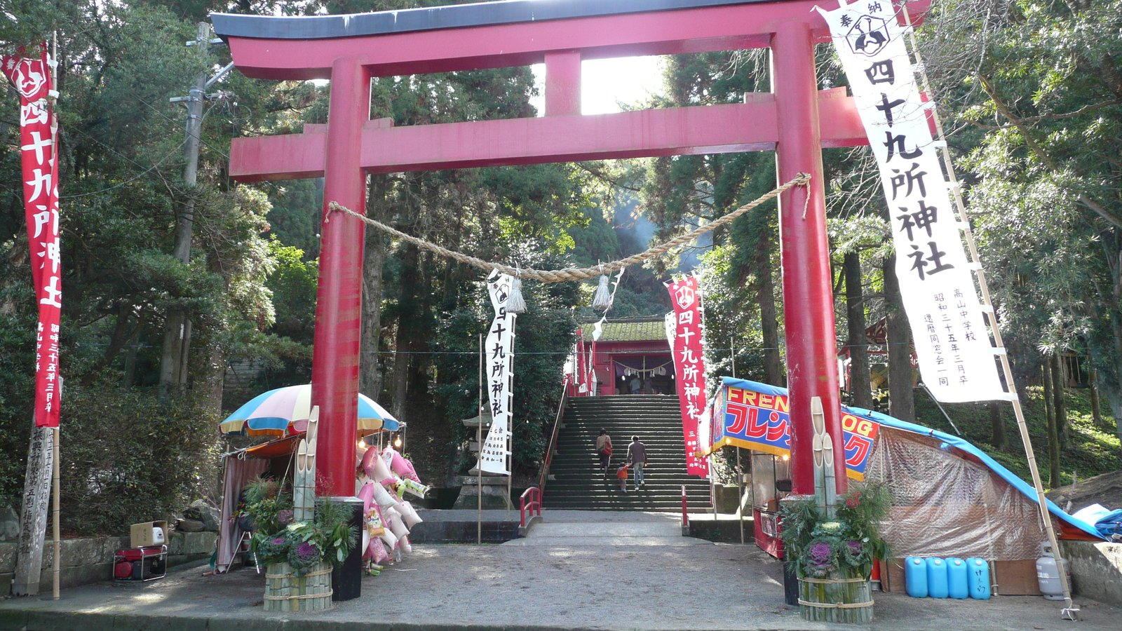 四十九所神社の朱塗りの鳥居。しめ縄が張られ、両脇に「四十九所神社」と書いた白い幟が立ち、奥の石段の上に社殿が見える