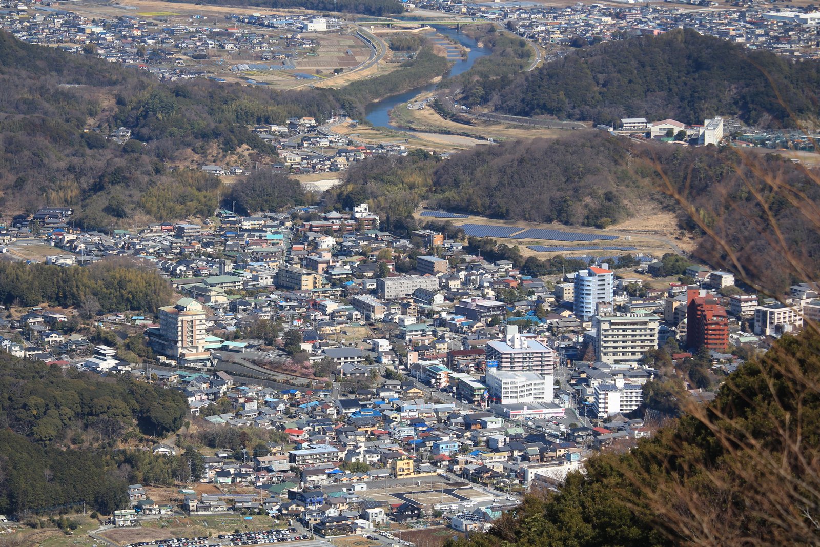 山の上から見下ろした伊豆長岡温泉の街並み。低い家並みの中にホテルらしい大きな建物が混じり、奥には川が蛇行し、周りを林の山が囲んでいる
