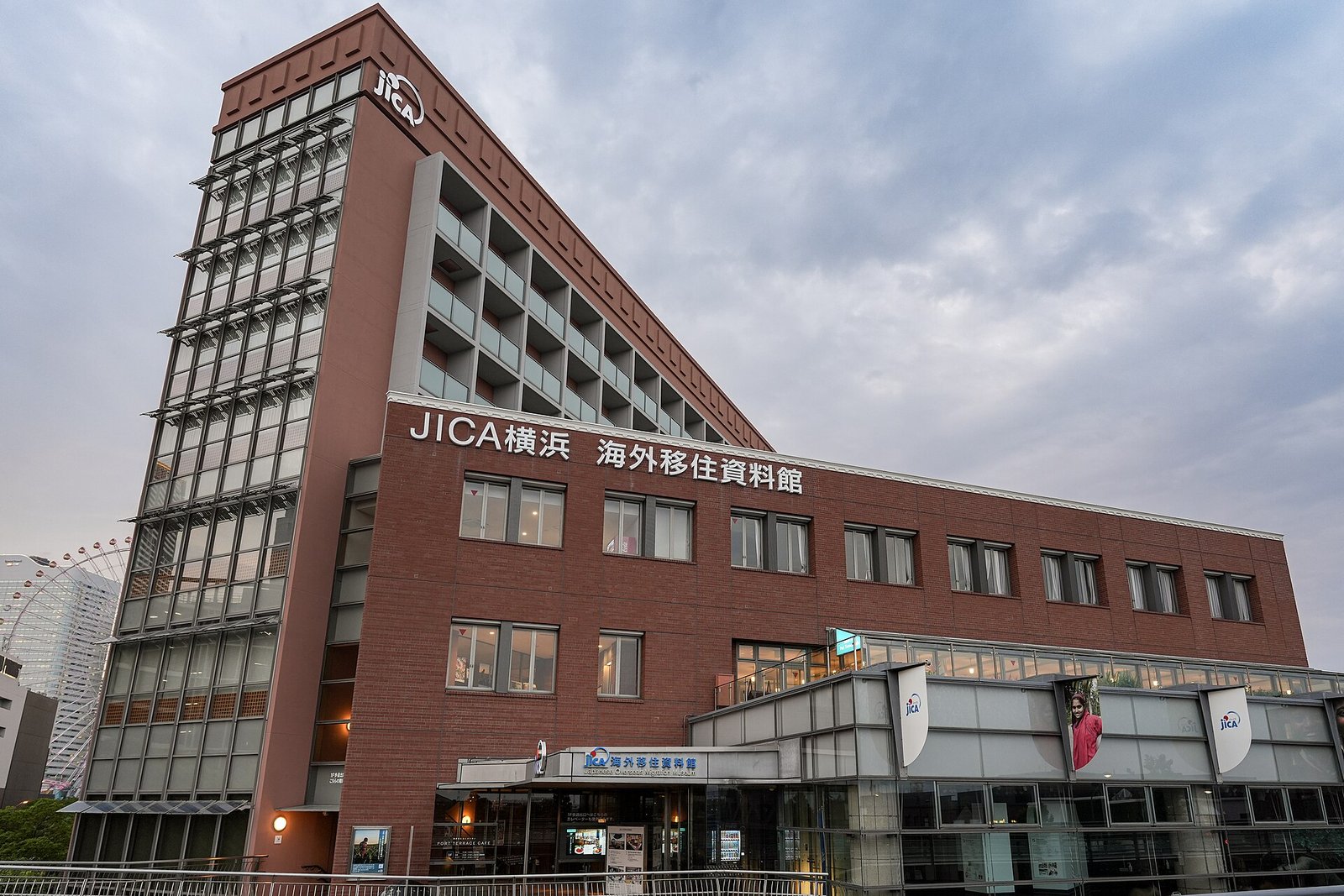 夕暮れのJICA横浜の建物外観。「JICA横浜 海外移住資料館」の看板があり、左手前に観覧車が見える