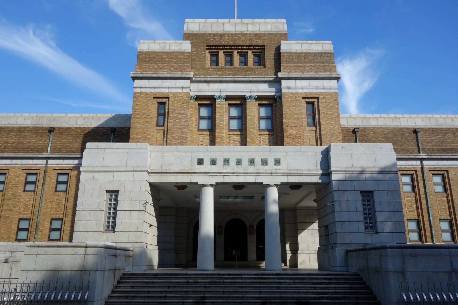 国立科学博物館 日本館（重要文化財）の正面玄関。花崗岩の車寄せと2本の円柱、その上に「国立科学博物館」の陽刻文字、背後に褐色タイル張りの塔屋が青空の下にそびえる