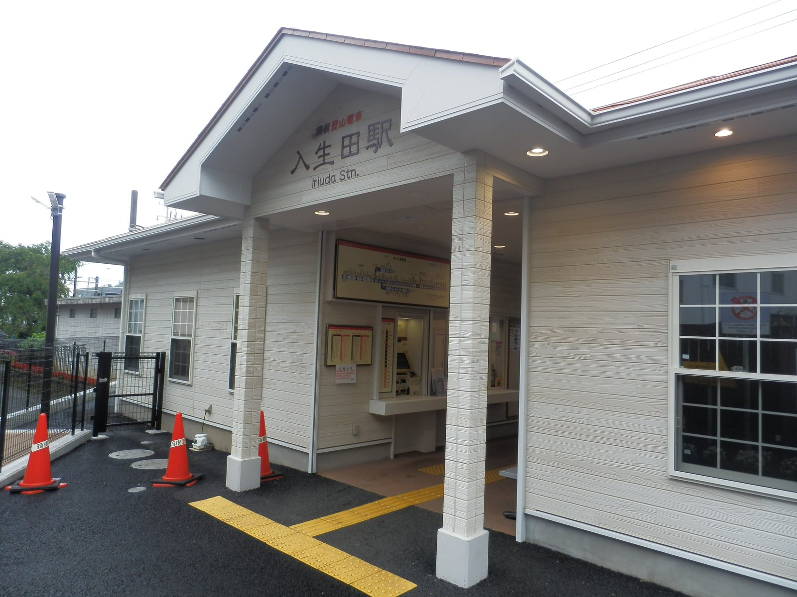 箱根登山鉄道の入生田駅の駅舎。白い板張りの平屋で、三角屋根の入口の上に「入生田駅 Iriuda Stn.」の文字、中に路線図と券売機が見える