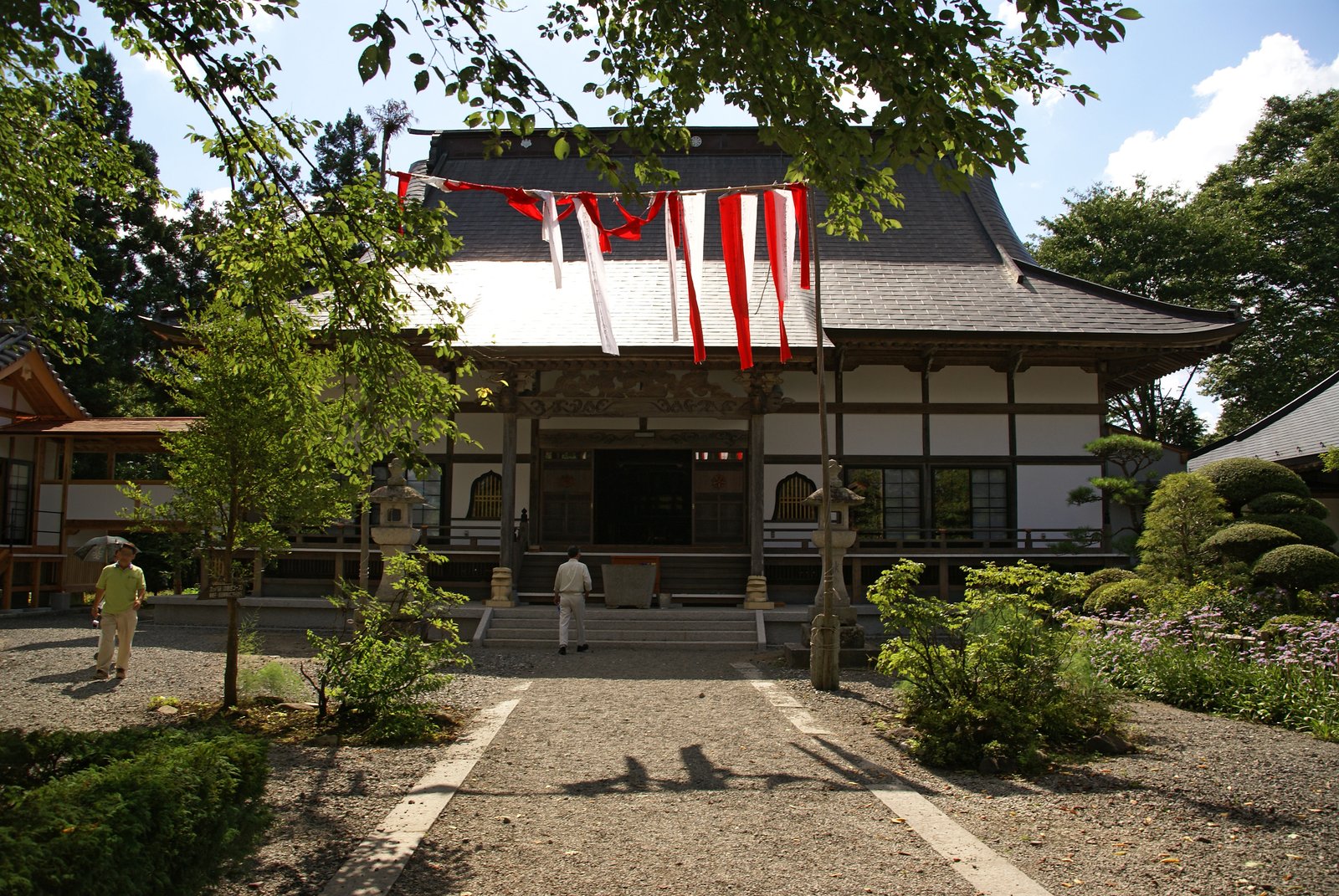 遠野市土淵町の常堅寺の本堂。白壁に黒い屋根の木造の建物で、正面に紅白の幕が張られ、砂利の参道の両側に石灯籠が立つ