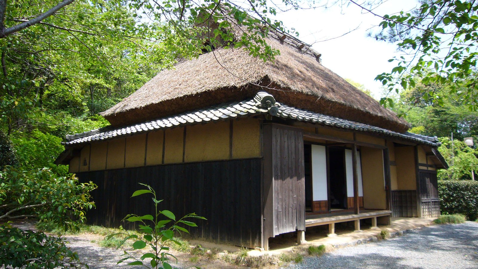 茅葺きの屋根の下に瓦の庇がついた柳田國男の生家。土壁と黒い板壁の平屋で、縁側の戸が開いている