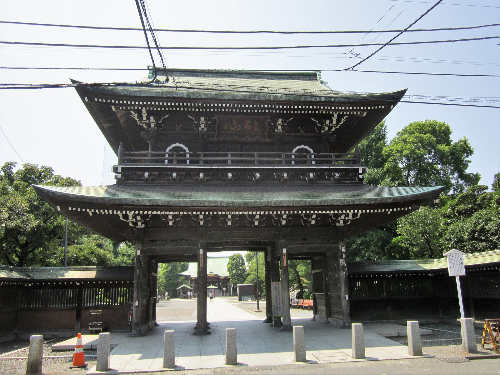 川崎大師の不動門。二層の屋根の木造の門で、門の奥に参道と本堂が見える