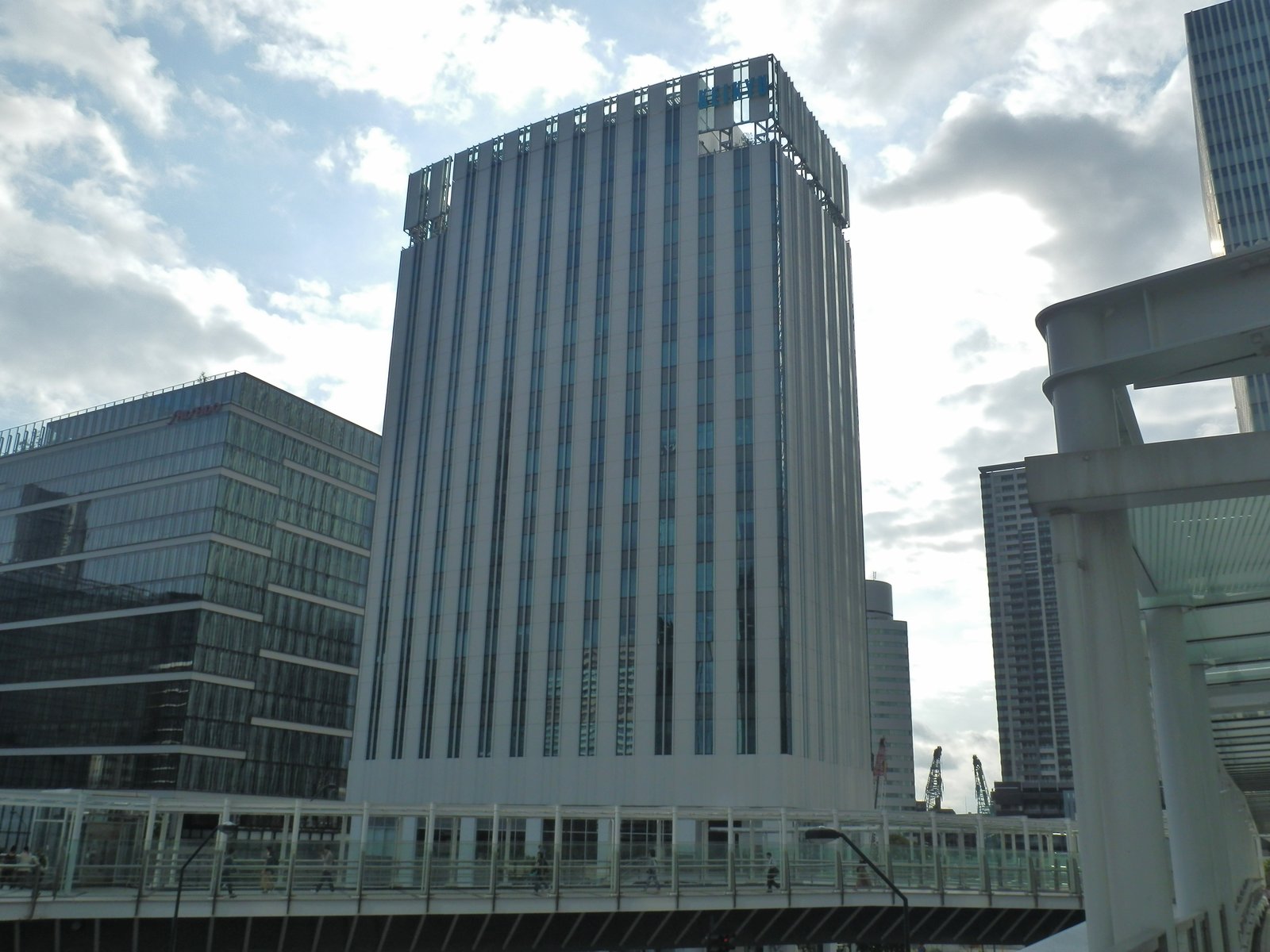 みなとみらいに建つ白い縦縞の高層ビル、京急グループ本社。手前をガラス屋根の歩道橋が横切る