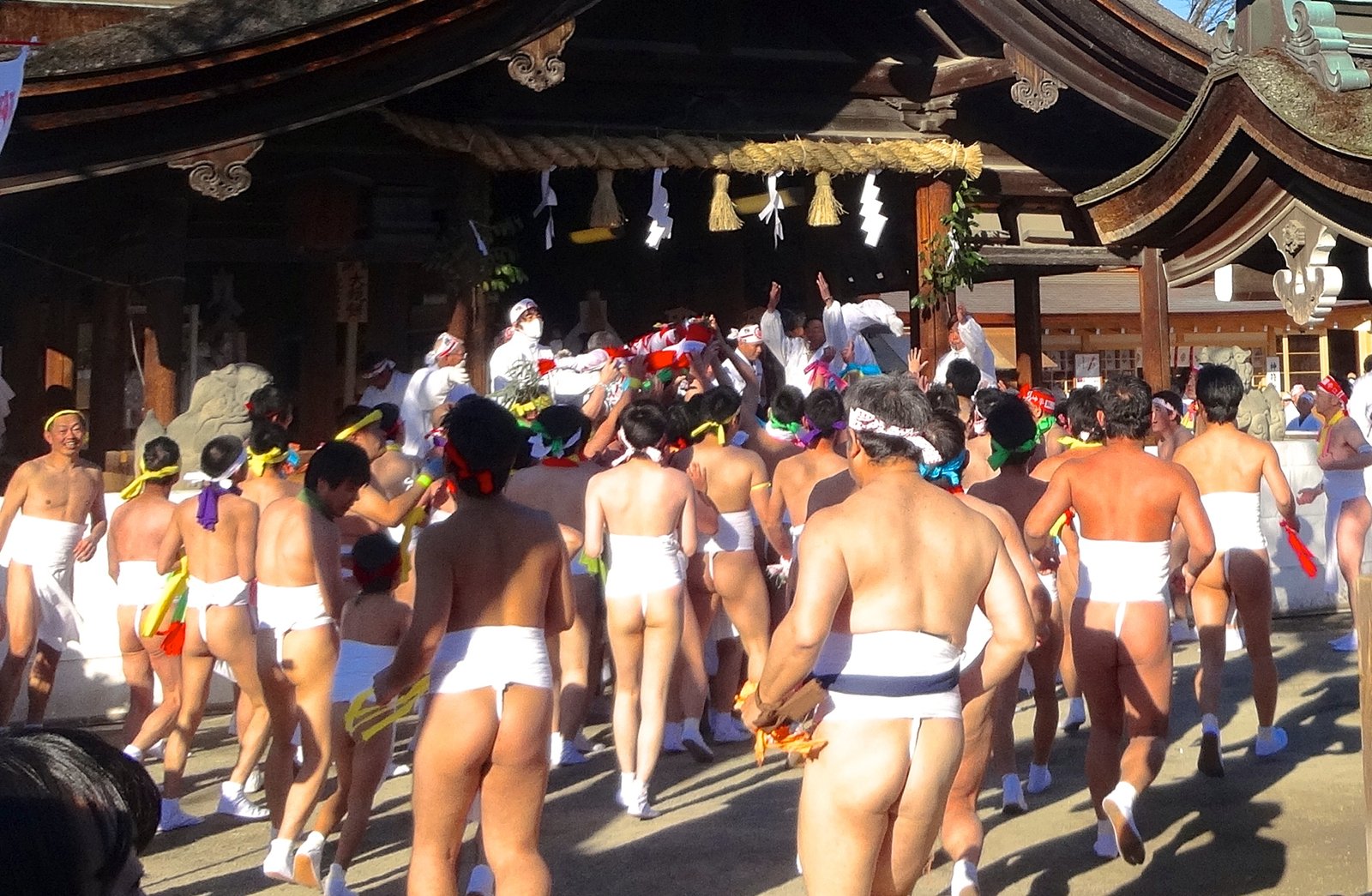 注連縄を張った社殿の前に駆け込む裸男たち。白いさらしに色のはちまきで、社殿の中に白い装束の人が並ぶ