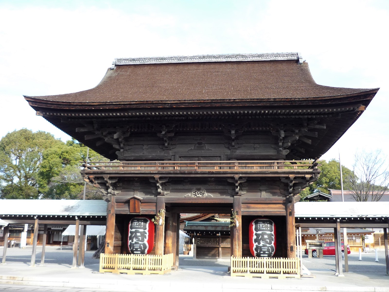 尾張大國霊神社の楼門。二層の大きな屋根の木造の門で、柱のあいだに提灯が下がっている