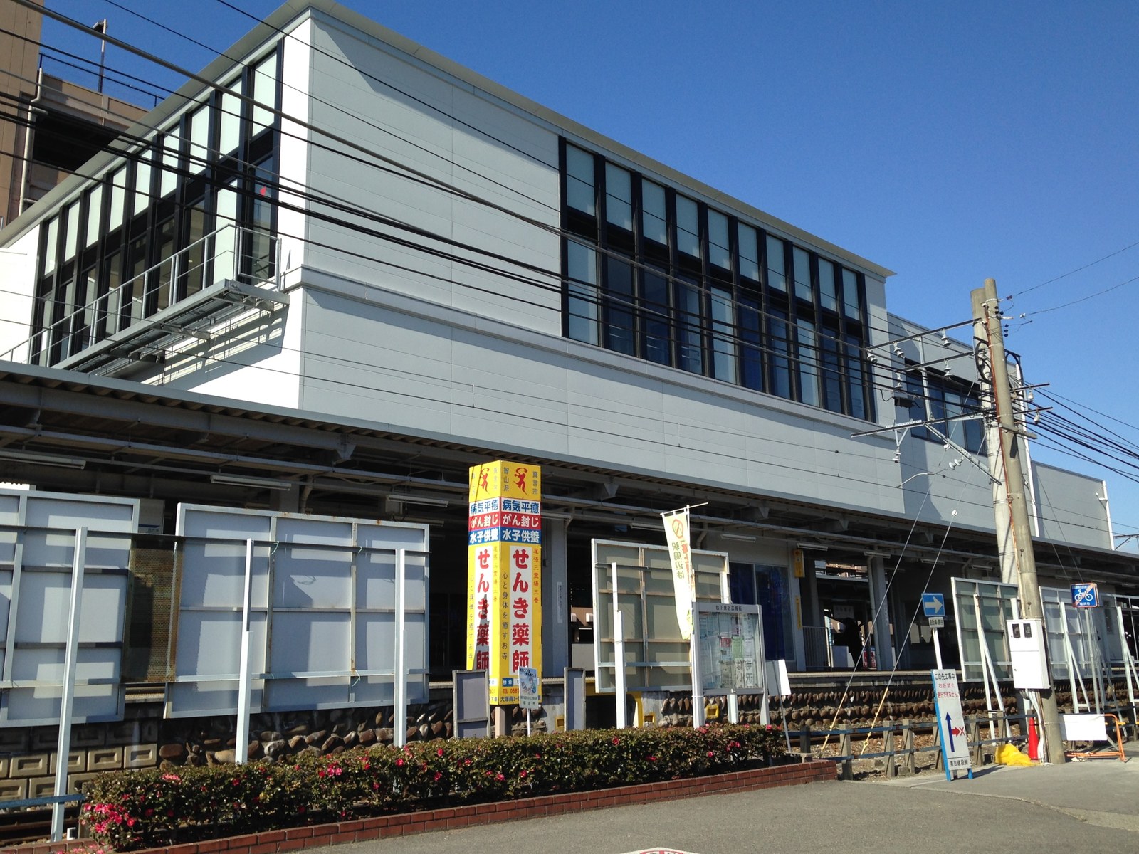 名鉄 国府宮駅の駅舎。線路をまたぐ白い橋上の建物で、手前に案内の看板が並んでいる