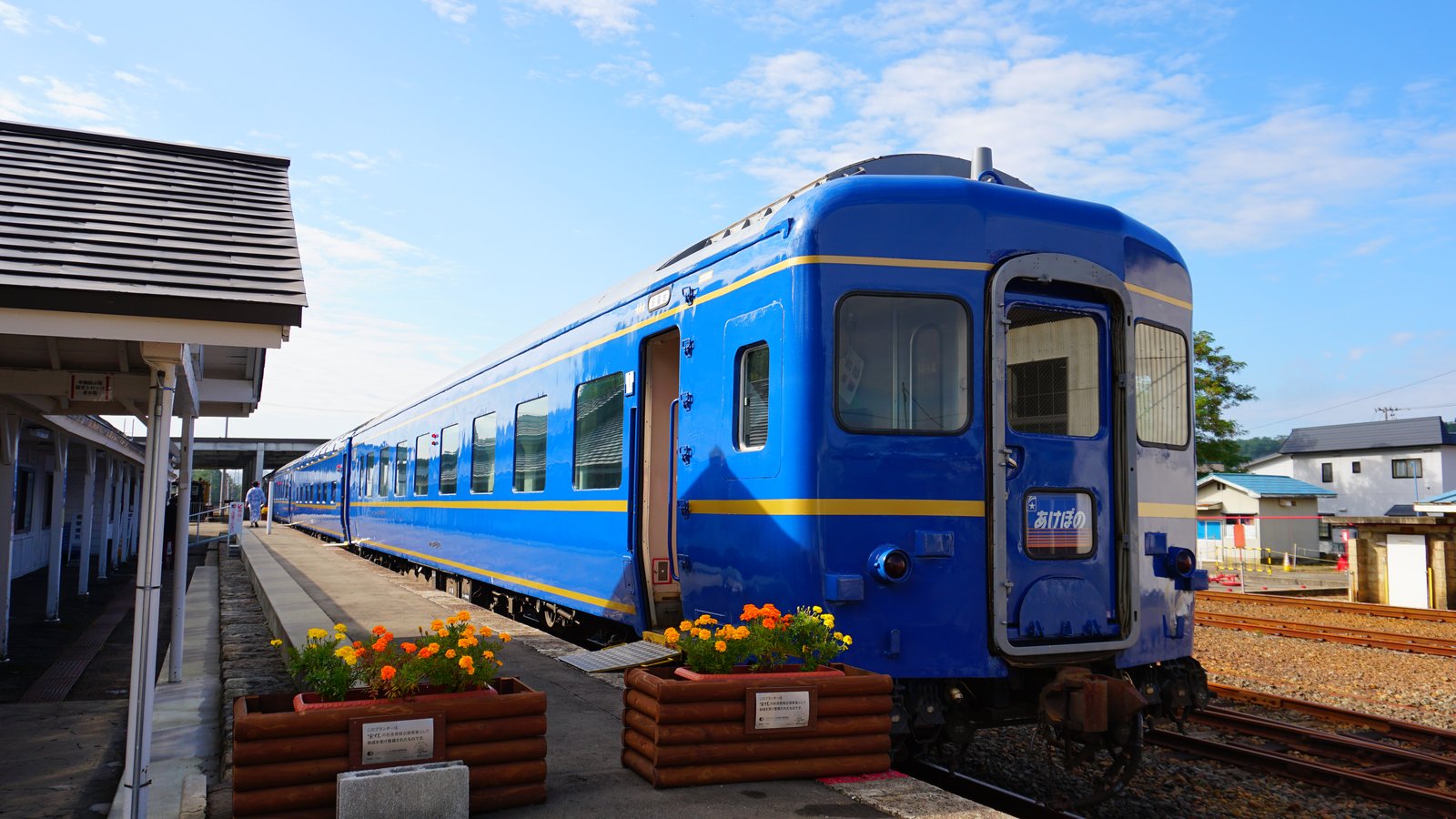 旧小坂駅のホームに停まる青い24系客車。最後尾に「あけぼの」のマークが付き、ホームにはマリーゴールドのプランターが並ぶ
