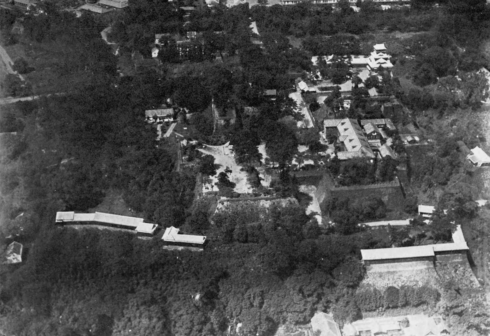 1931年の熊本城を上空から写した白黒写真。木々に囲まれた石垣の上に櫓と長い塀が並ぶ