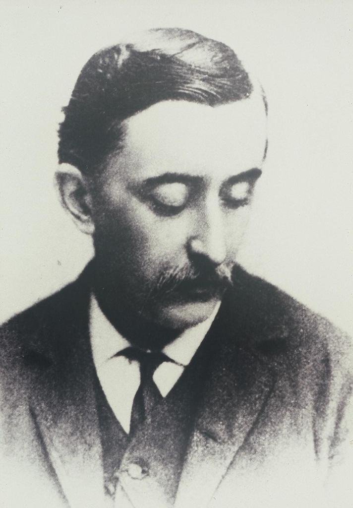 小泉八雲(ラフカディオ・ハーン)の肖像写真。口ひげをたくわえ、目を伏せて顔を右へ向け、背広に襟の高い白いシャツと黒いネクタイを着けている