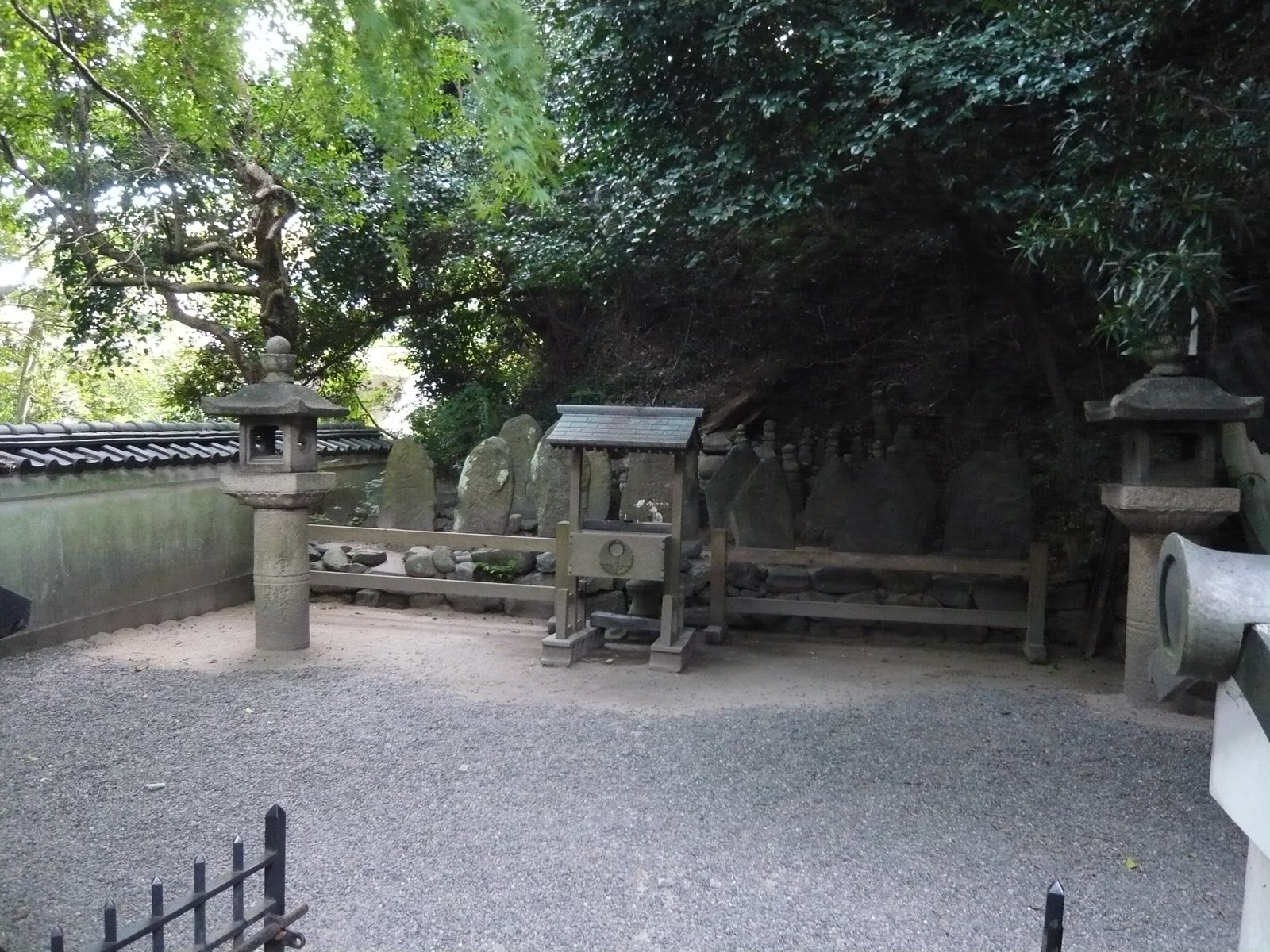 赤間神宮の七盛塚。木の柵の奥に自然石の墓石が十数基並び、手前に小さな屋根の付いた賽銭箱と石灯籠が立つ