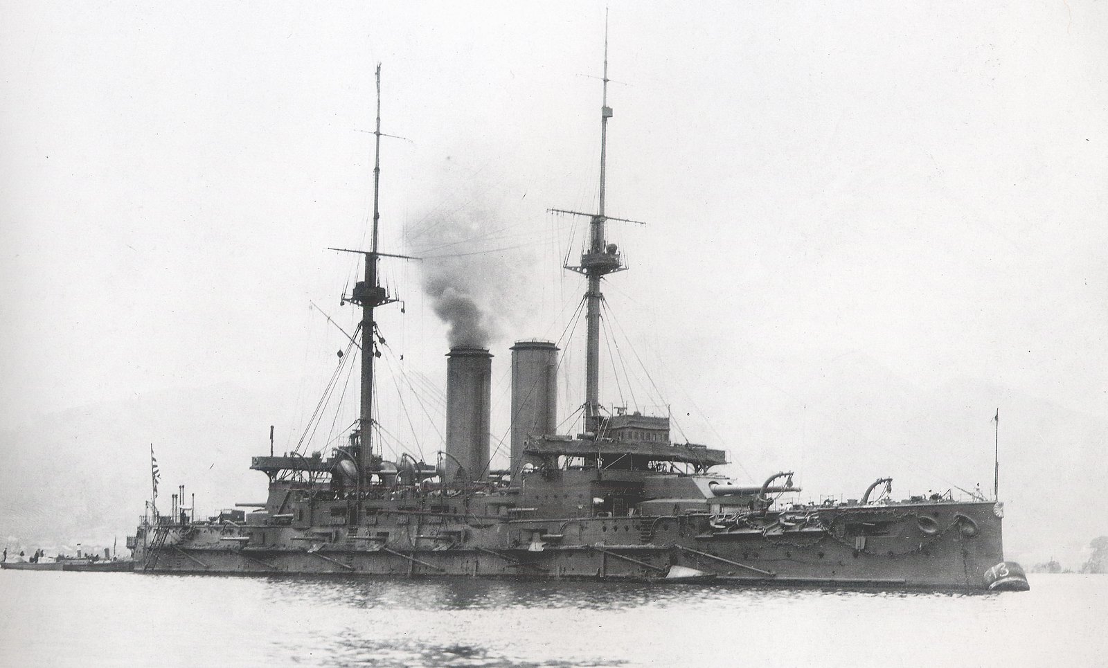 白黒の写真。海に浮かぶ戦艦「三笠」を横から写したもので、2本のマストのあいだに煙突が並び、煙が上がっている