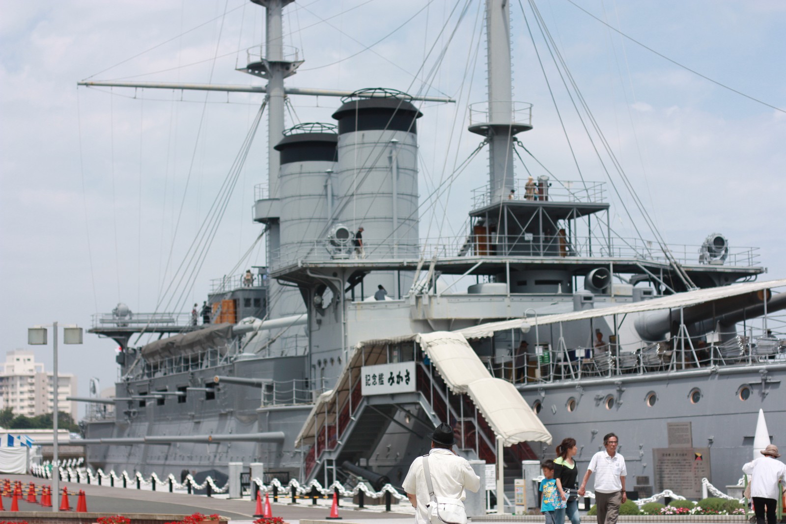 横須賀・三笠公園に係留された記念艦「三笠」の全景。3本の煙突と2本のマスト、主砲、舷梯の「記念艦みかさ」の看板、見学者が写る