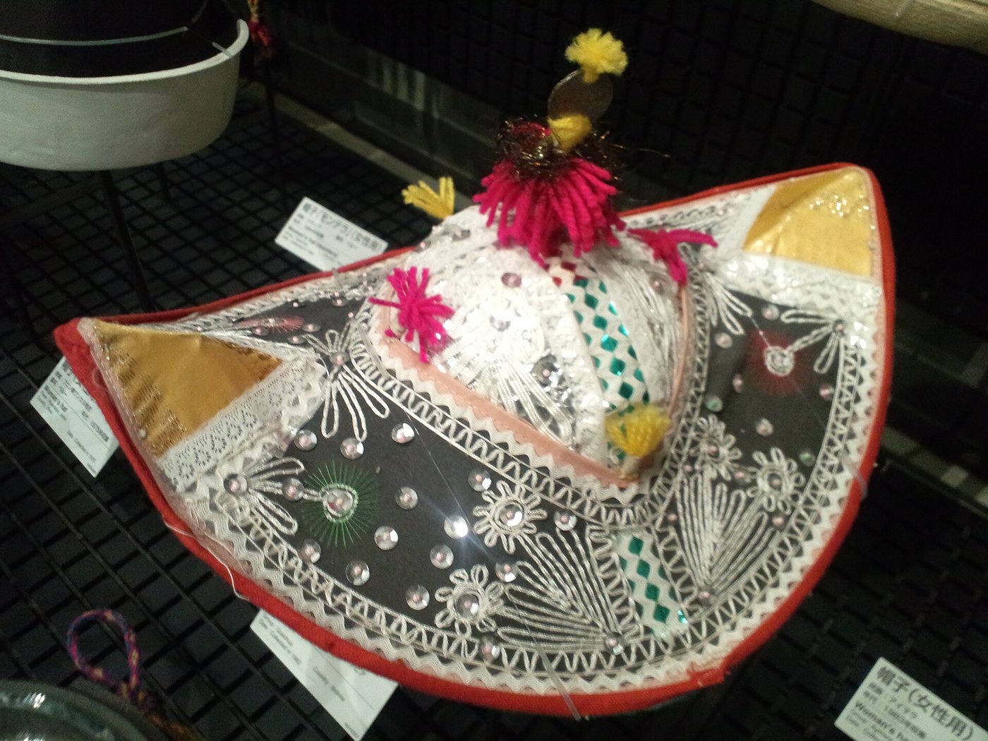 刺繍とスパンコールで飾られた帽子。赤い縁取りに白いレース模様、頂部にピンクと黄色の房飾りが付いている
