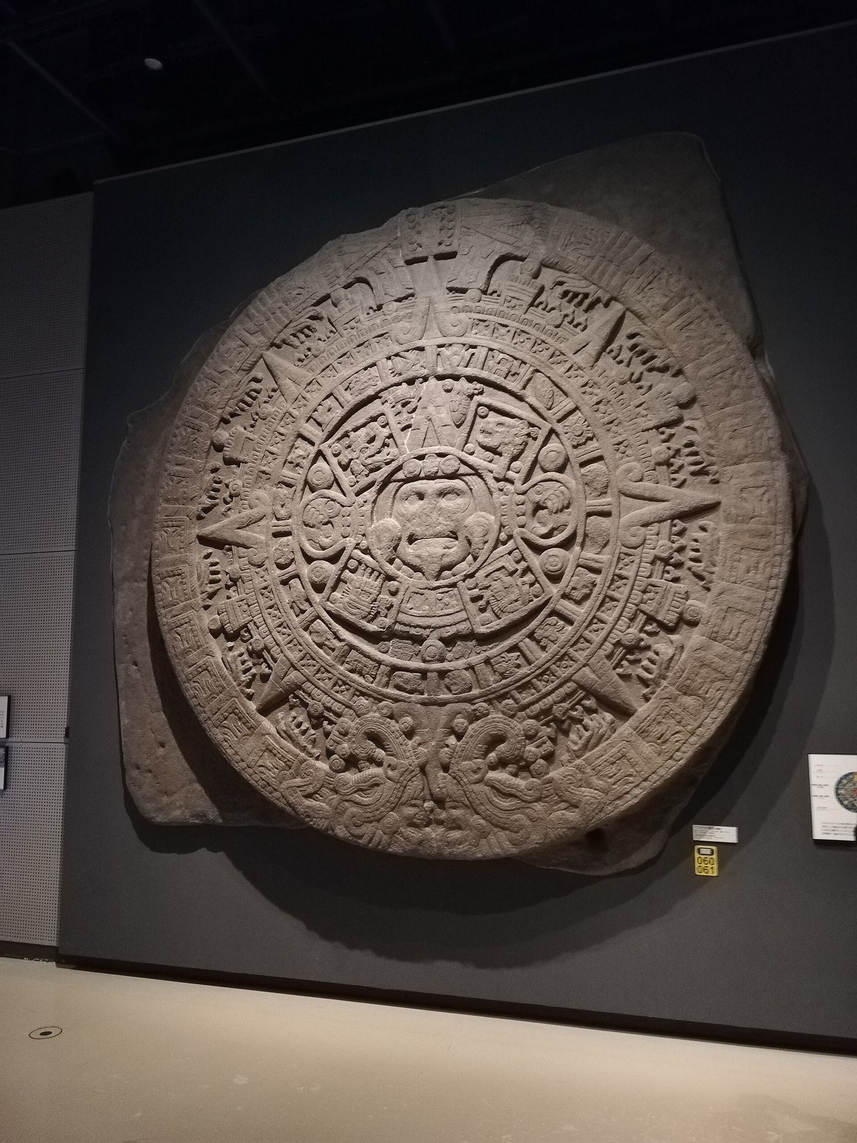 国立民族学博物館アメリカ展示場に展示されたアステカ暦石のレプリカ。円盤状の石に幾何学模様と顔の彫刻が刻まれている