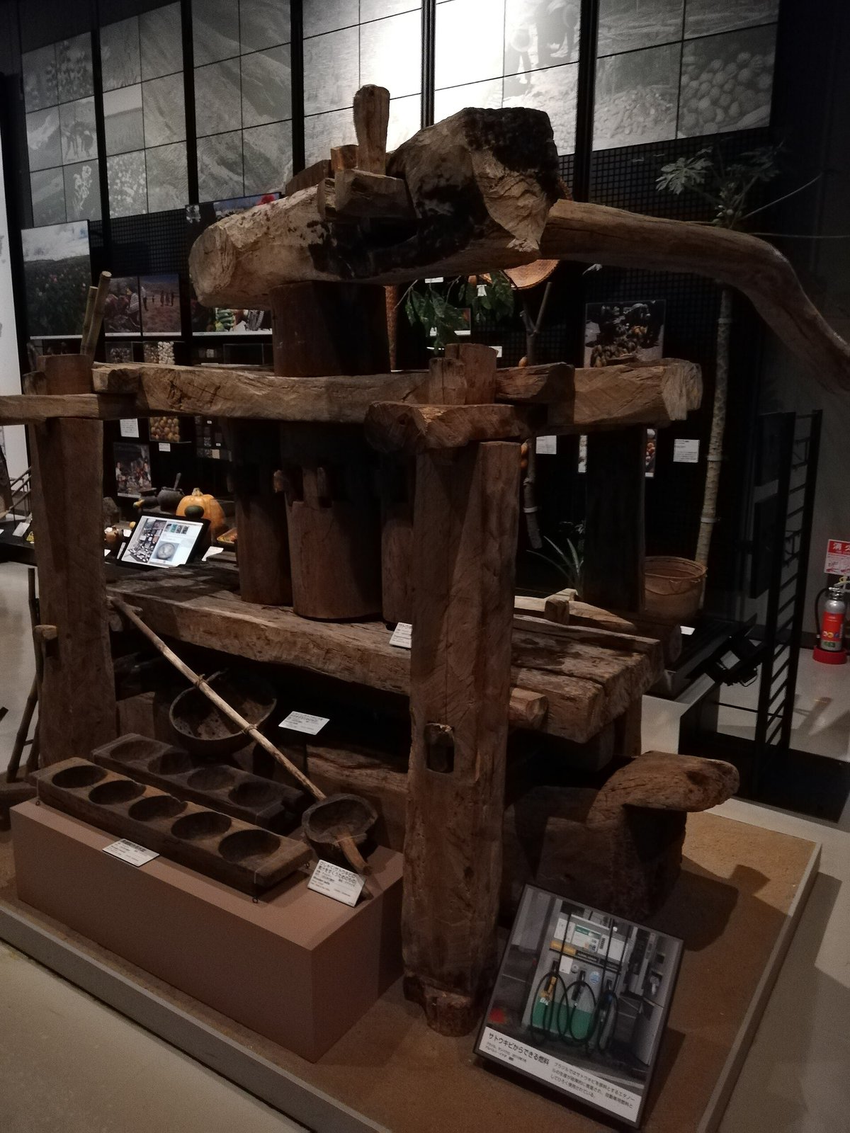 木製のサトウキビ圧搾機。太い柱と横木を組んだ構造で、手前に木製の型と壺が置かれている