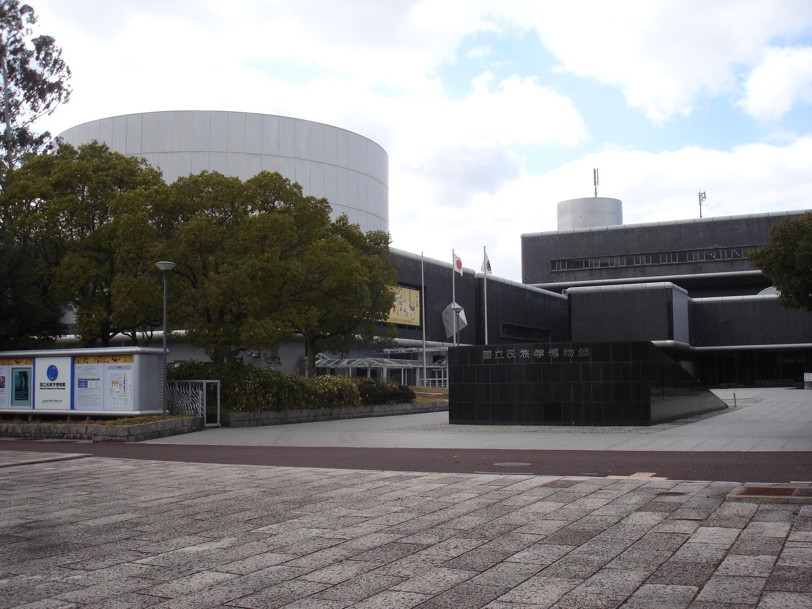 国立民族学博物館の正面。館名を刻んだ黒い石の壁の奥に暗い灰色の本館、左奥に円筒形の白い建物