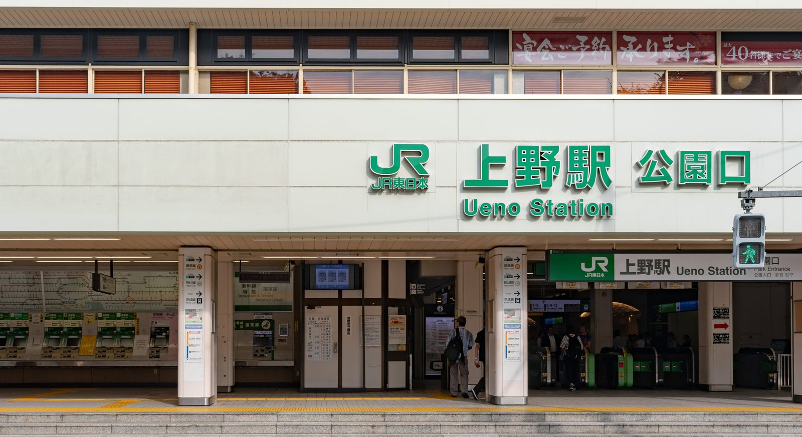 JR上野駅の公園口の駅舎。白い外壁の上部に緑の文字で「上野駅 公園口」と「Ueno Station」の表示があり、その下に改札と券売機が並ぶ