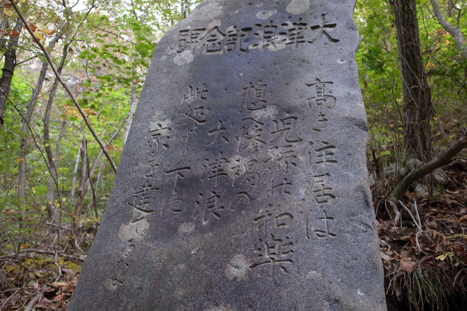 林の中に立つ自然石の碑。「大津浪記念碑」の題と、「高き住居は児孫の和楽 想へ惨禍の大津浪 此処より下に家を建てるな」の文字が縦書きで彫られている