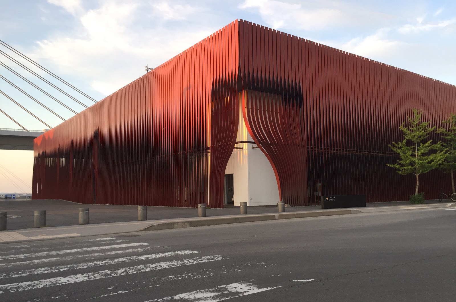 ねぶたの家 ワ・ラッセの外観。赤い鋼板の帯で覆われた四角い建物で、入口のところだけ帯がめくれている