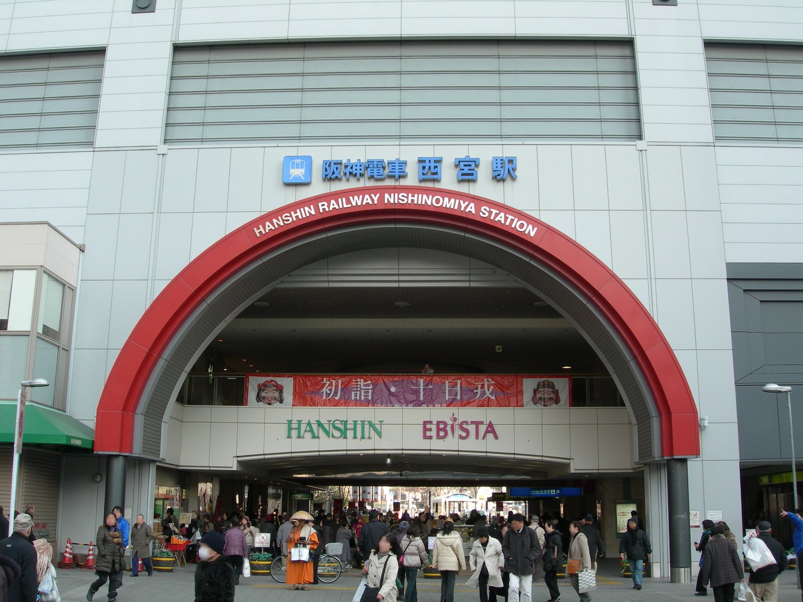 赤いアーチの入口を持つ阪神電車西宮駅の駅ビル。アーチの中に「初詣・十日戎」の横断幕が掛かり、下を大勢の人が行き交う