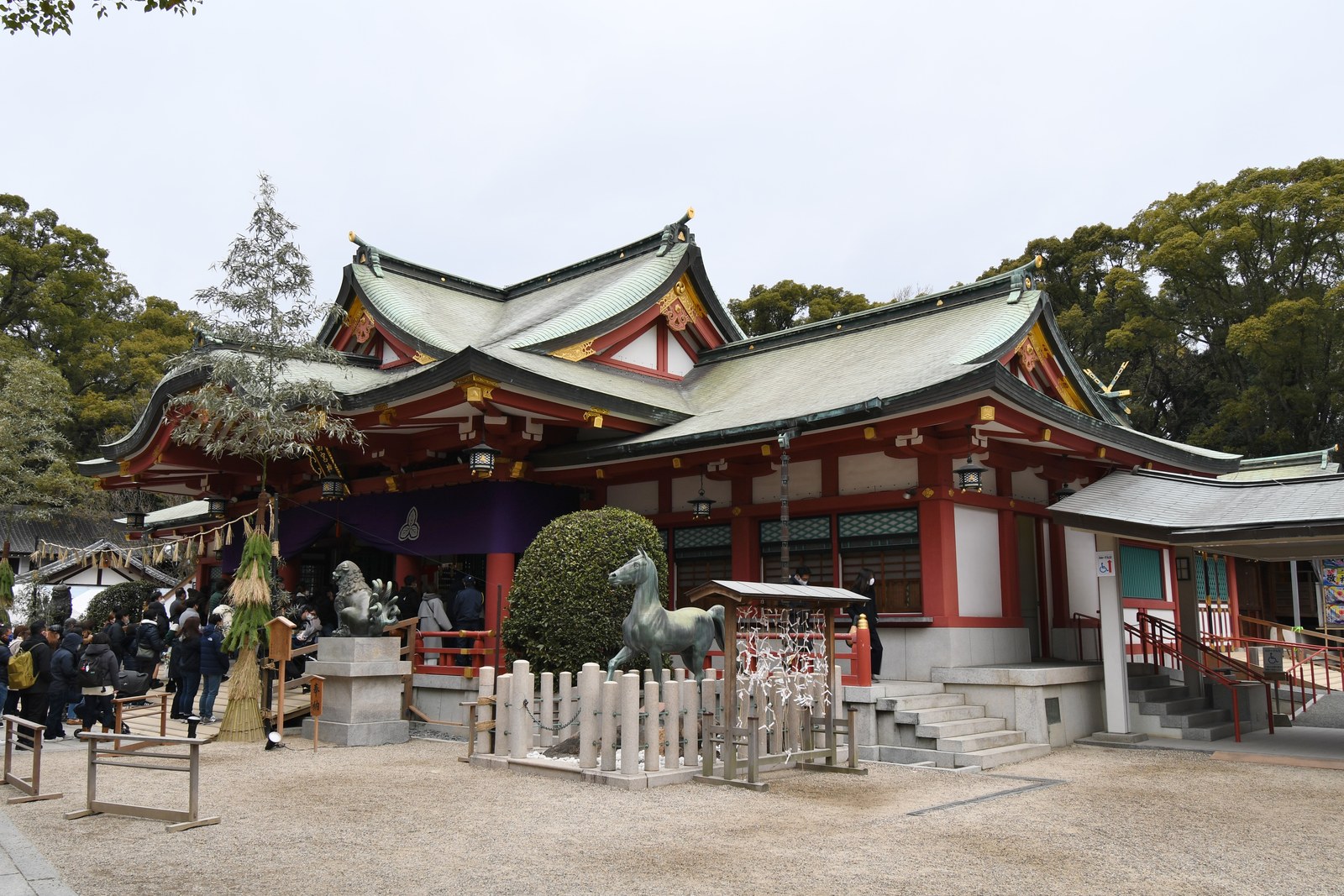 西宮神社の拝殿。朱塗りの柱に緑青色の屋根が 3 つ連なり、前に神馬の像がある