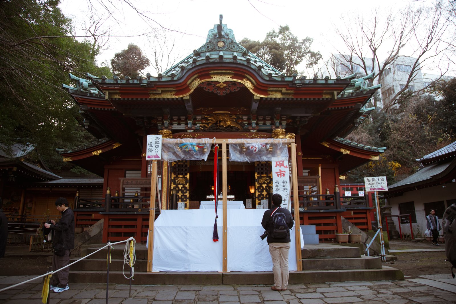 王子稲荷神社の社殿。朱塗りの柱と緑青の屋根、正面に「凧市 初午祭」の看板と白い幕、参道にロープが張られている
