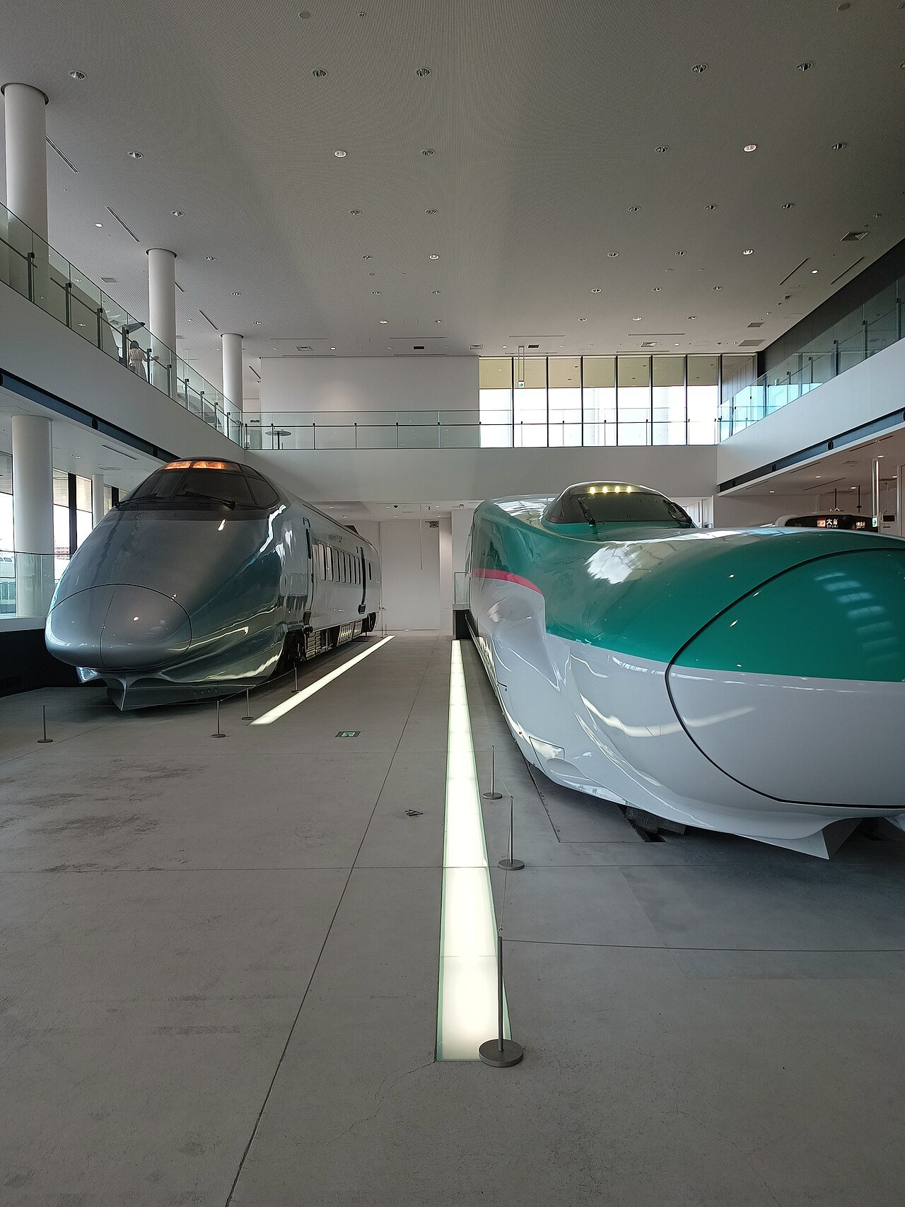 南館の新幹線展示ホール。吹き抜けの明るい空間に、銀色の新幹線車両と、緑と白の新幹線車両の先頭部が並ぶ