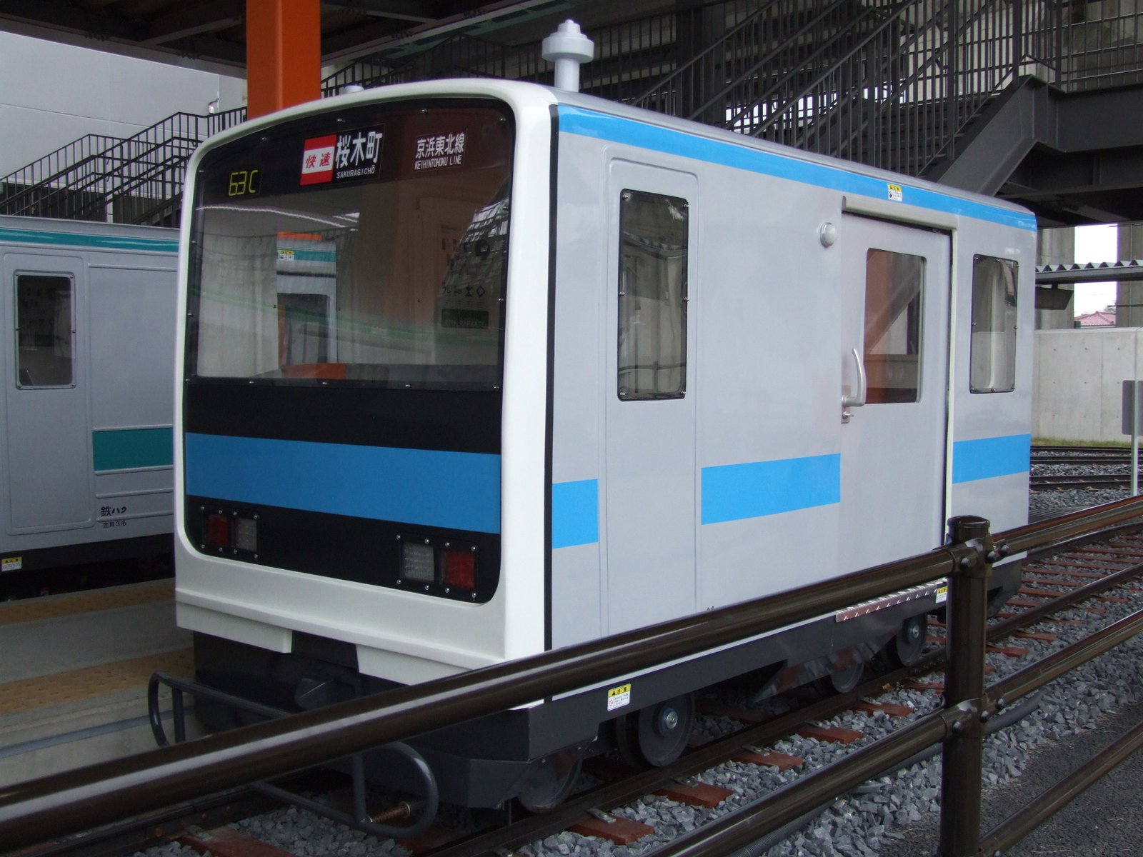 ミニ運転列車の車両。京浜東北線カラーの帯を巻いた白い車体で、線路上に停まっている