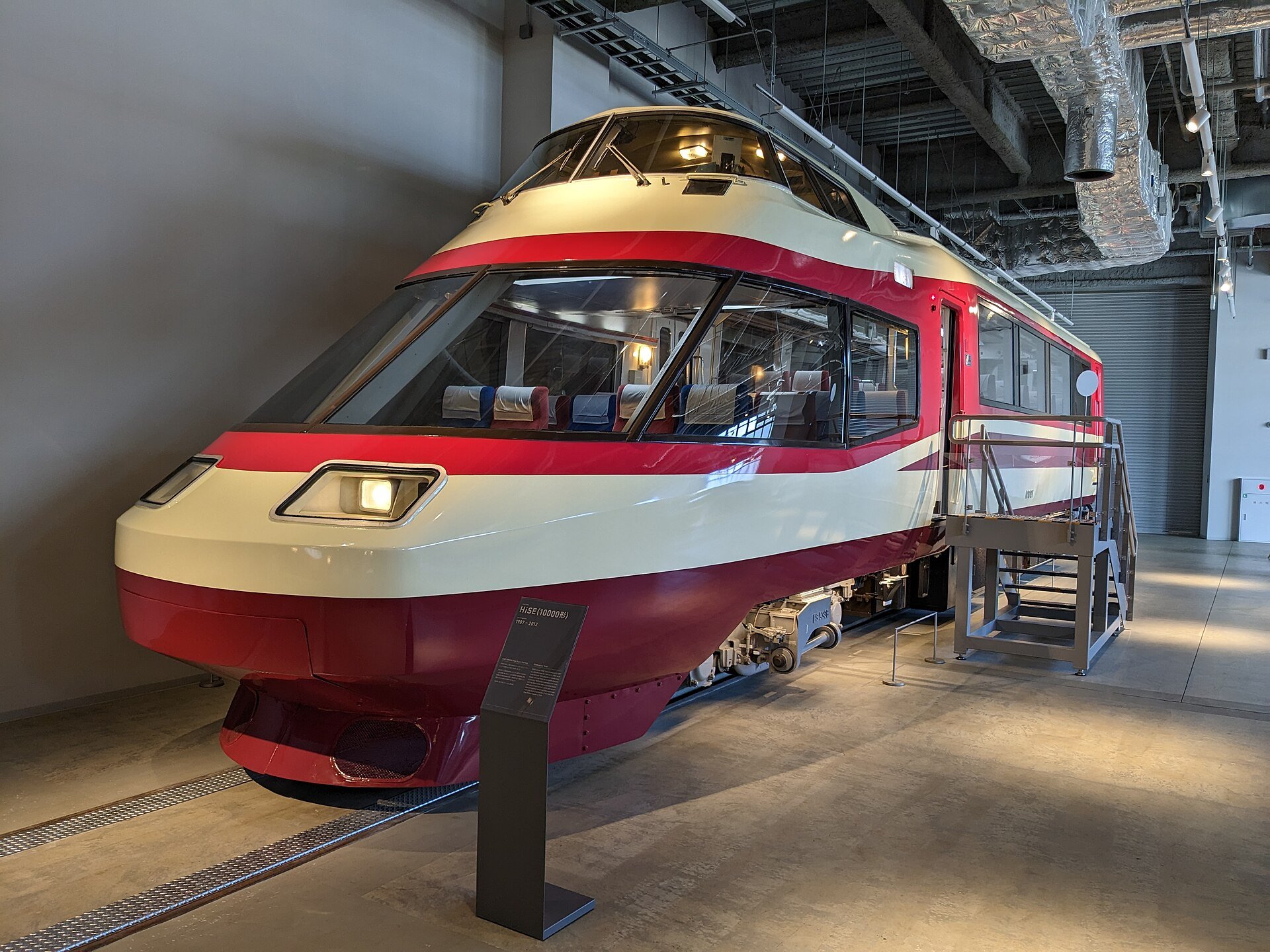 展示されているHiSE(10000形)の先頭車、赤と白の流線形の車体に「HiSE(10000形)」の解説板